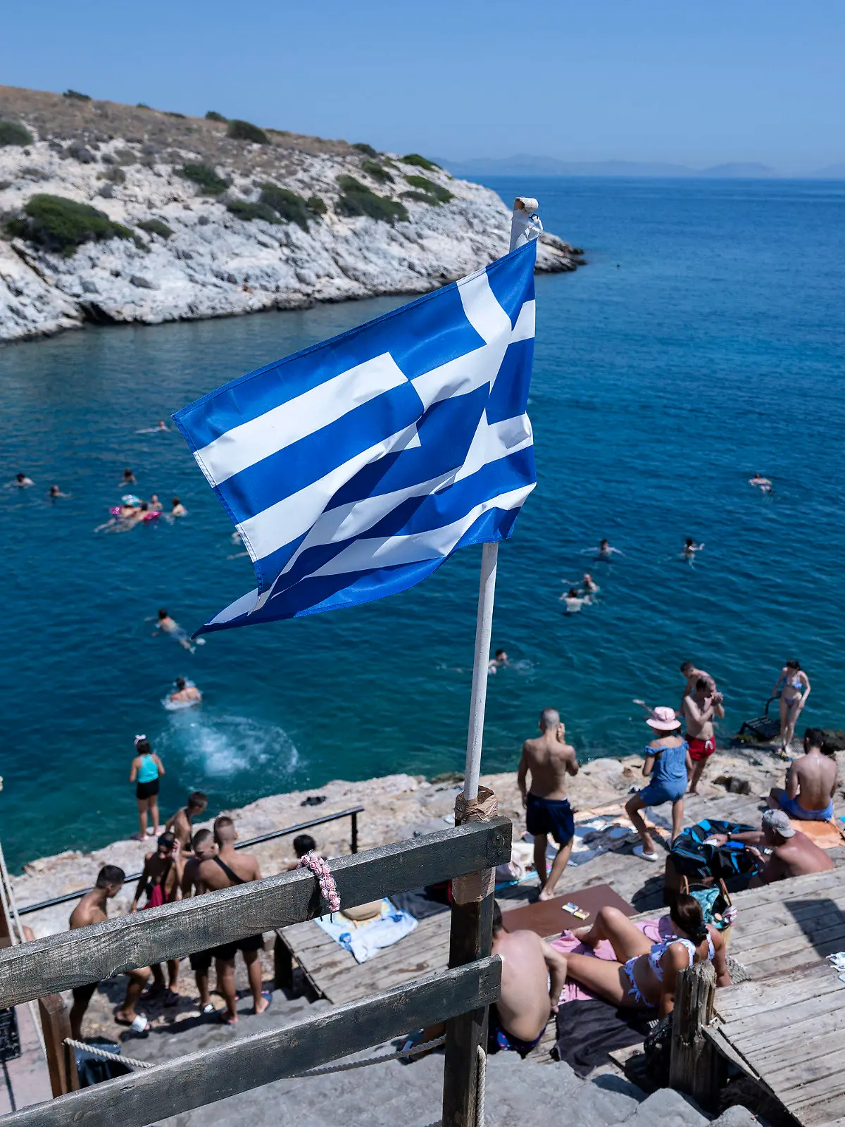22.07.2023, Griechenland, Athen: Schwimmer sitzen auf Felsen am Meer im Vorort Vioulagmeni, südöstlich von Athen. Es wird erwartet, dass sich die Hitze in Griechenland im Laufe des Wochenendes verstärkt und sich 44 Grad Celsius nähert. Das ganze Land soll bis Ende Juli eine weitere Hitzewelle erleben. Foto: Yorgos Karahalis/AP/dpa/dpa +++ dpa-Bildfunk +++