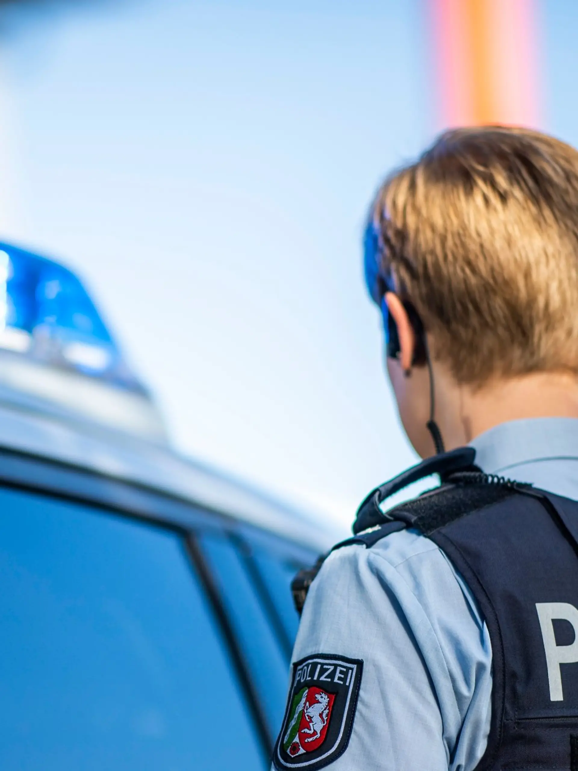 Eine Polizistin steht vor einem Streifenwagen.