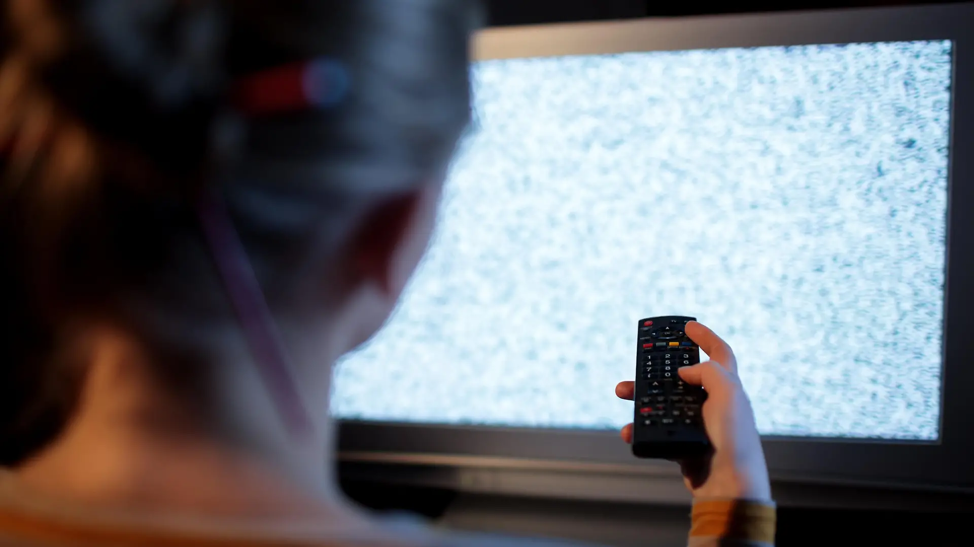 Back view of woman with remote control in front of TV set with noise on the screen