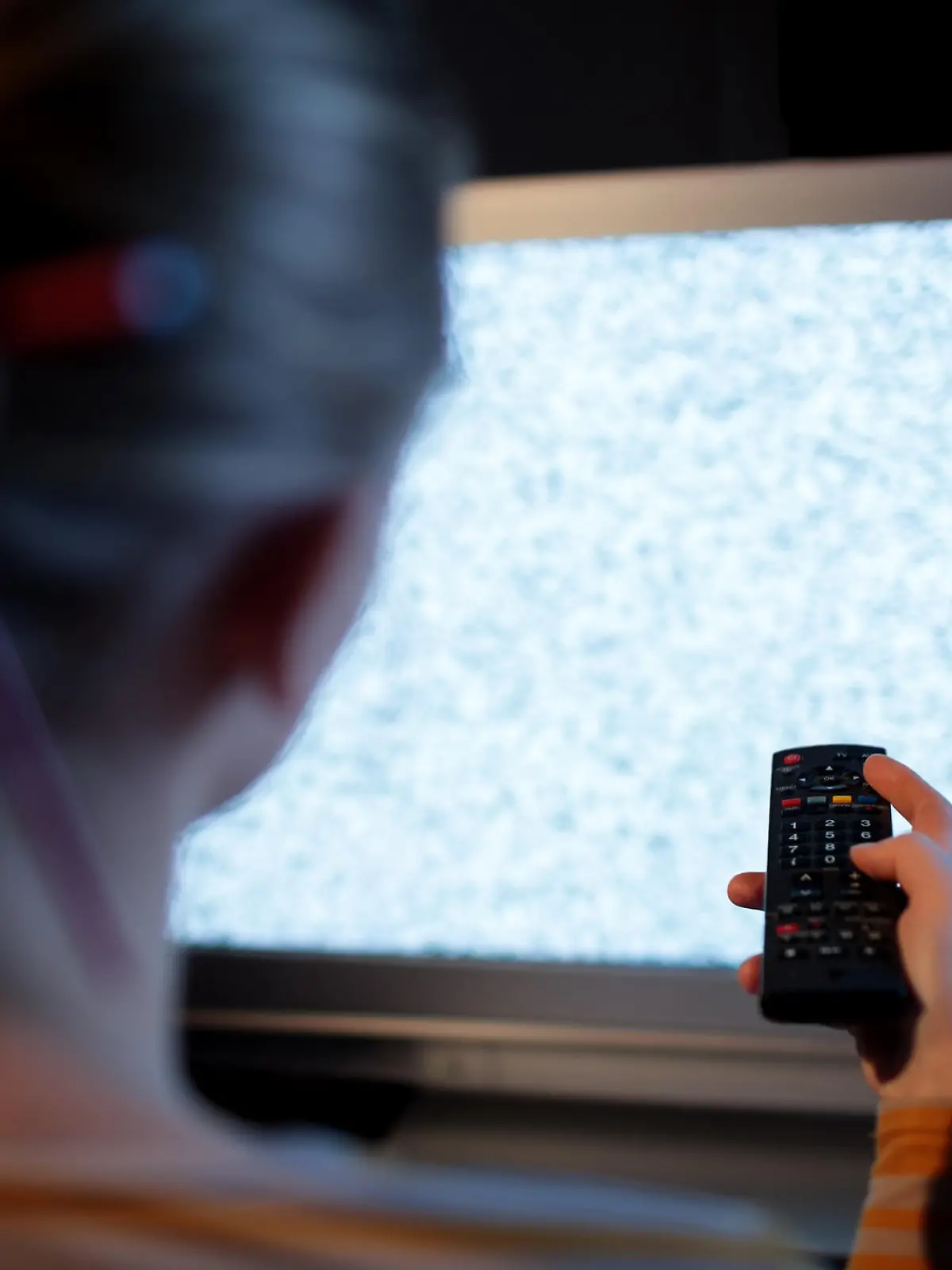 Back view of woman with remote control in front of TV set with noise on the screen
