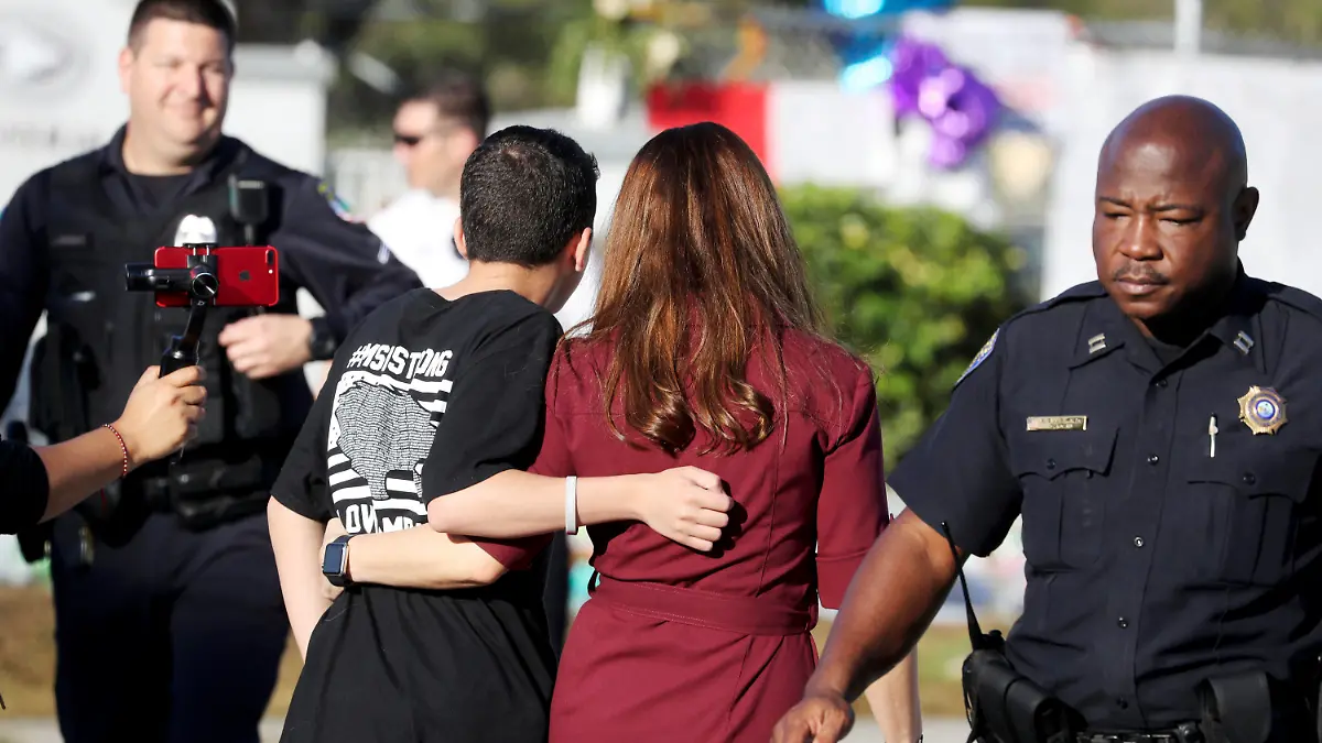 28.02.2018, USA, Florida, Parkland: Ein Schüler der Marjory Stoneman Douglas High School geht Arm in Arm mit seiner Mutter auf das Schulgelände, das von mehreren Polizisten bewacht wird. Nach dem Massaker in Parkland kehren die Schüler an die betroffene High School zurück. Foto: Mike Stocker/South Florida Sun-Sentinel/AP/dpa +++ dpa-Bildfunk +++