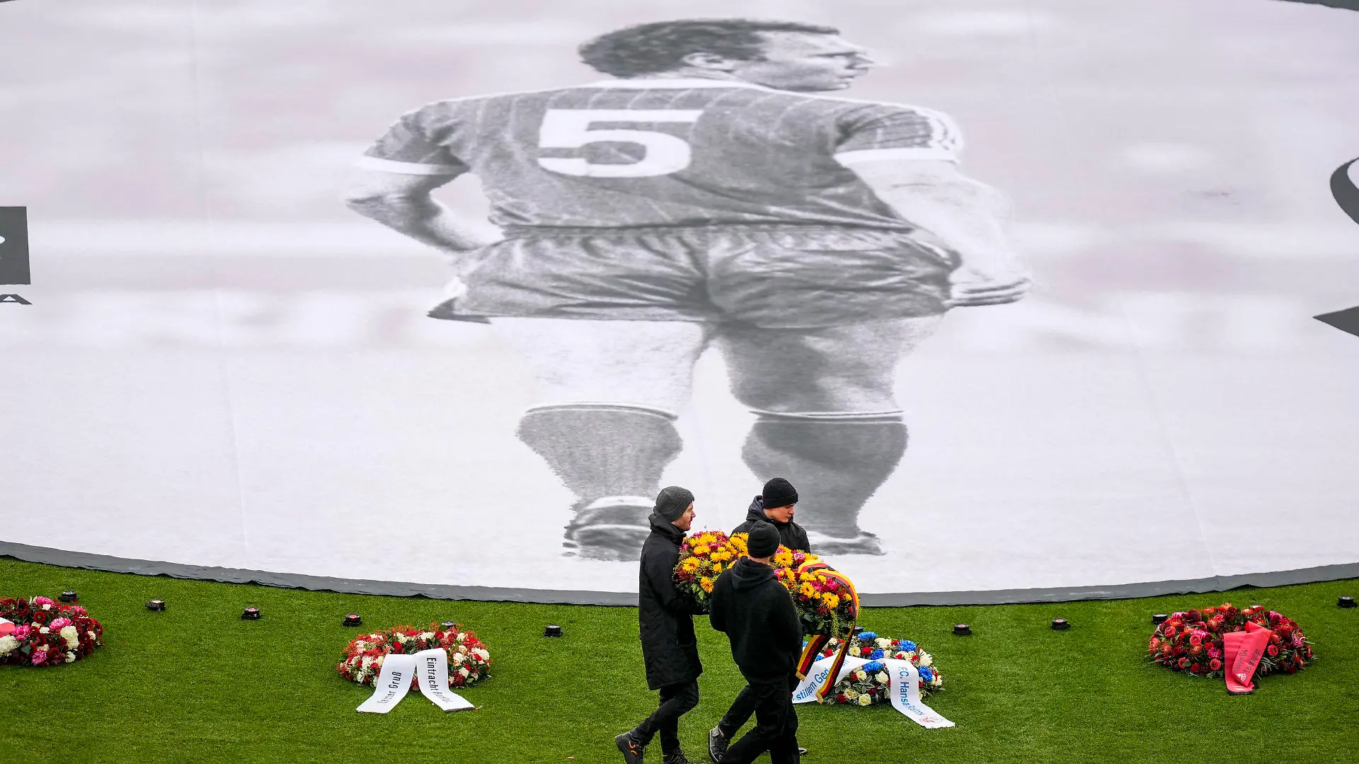 People place flower wreaths around a photograph of Bayern and Germany legend Franz Beckenbauer on the pitch of the Allianz Arena in Munich, Germany, Friday, Jan. 19, 2024, before a memorial service. Franz Beckenbauer, a club legend for Bayern as a player, coach and president, whose death at the age of 78 has prompted tributes from across the soccer world, has left a particularly deep impression on Bayern the team where he spent so much of his decades-long career. (AP Photo/Matthias Schrader)