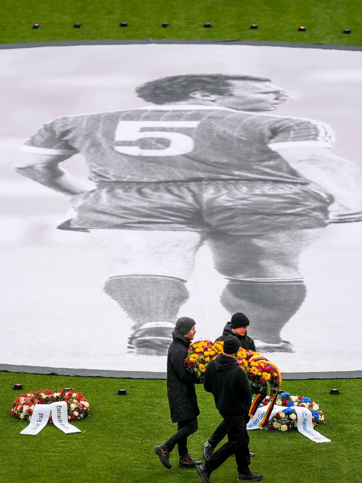 People place flower wreaths around a photograph of Bayern and Germany legend Franz Beckenbauer on the pitch of the Allianz Arena in Munich, Germany, Friday, Jan. 19, 2024, before a memorial service. Franz Beckenbauer, a club legend for Bayern as a player, coach and president, whose death at the age of 78 has prompted tributes from across the soccer world, has left a particularly deep impression on Bayern the team where he spent so much of his decades-long career. (AP Photo/Matthias Schrader)