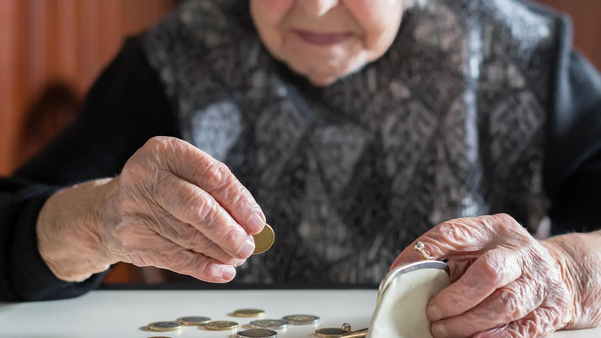 Elderly 95 years old woman sitting miserably at the table at home and counting remaining coins from the pension in her wallet after paying the bills.