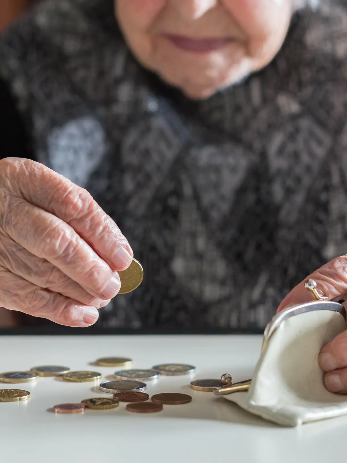 Elderly 95 years old woman sitting miserably at the table at home and counting remaining coins from the pension in her wallet after paying the bills.