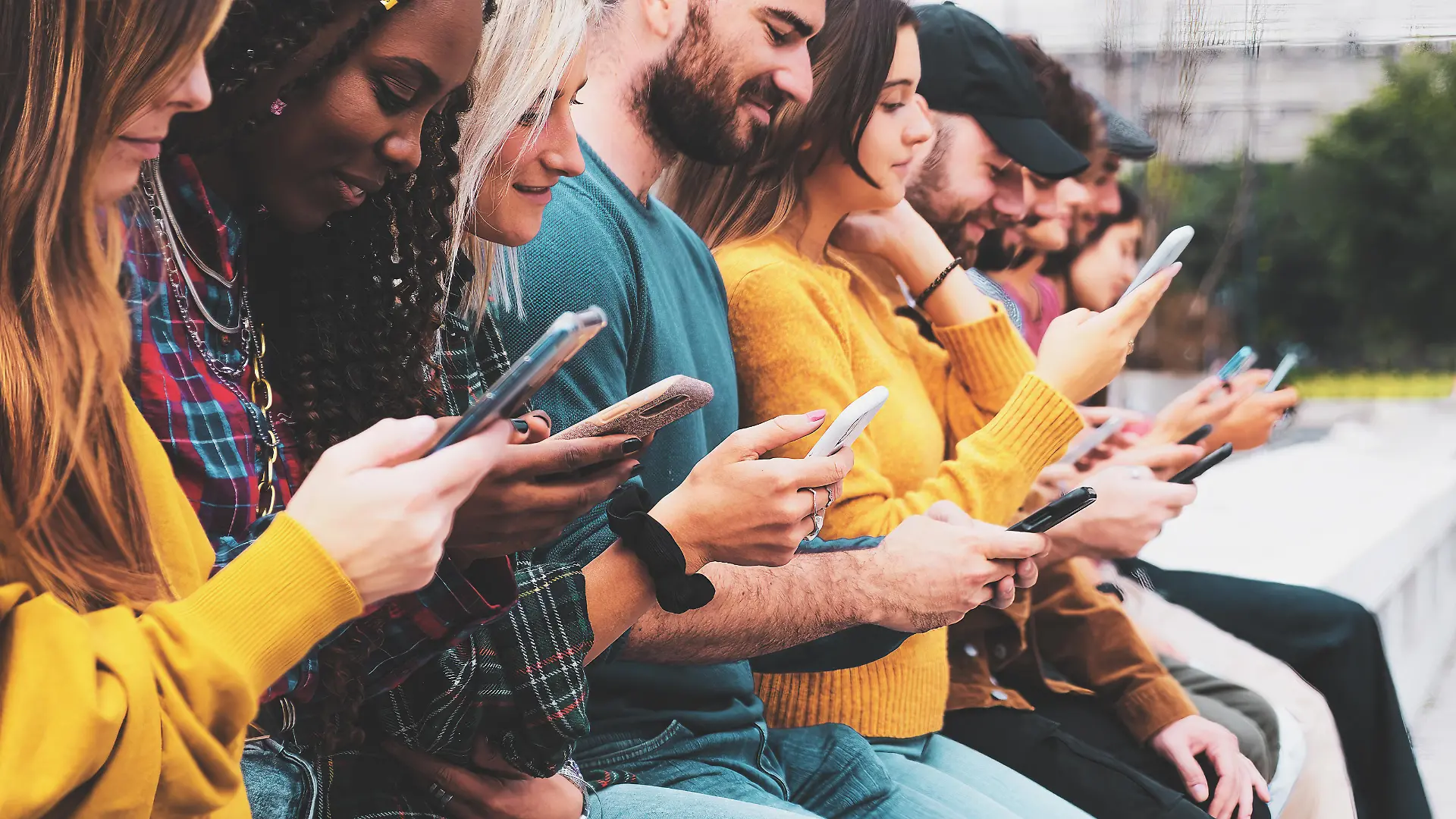 Closeup group of interracial gen z hipsters friends Sitting outdoors typing on modern smartphone devices.
Millenial people swiping on touch screens and using the internet concept