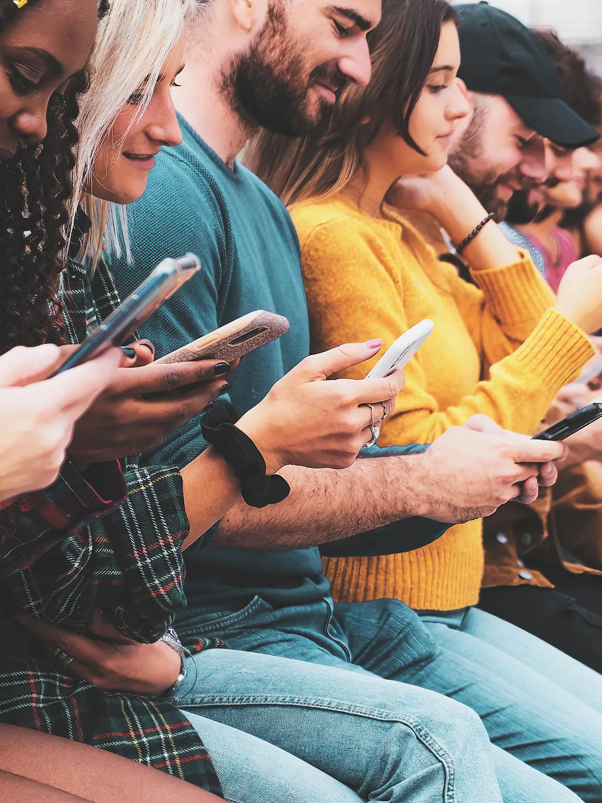 Closeup group of interracial gen z hipsters friends Sitting outdoors typing on  modern smartphone devices. 
Millenial people swiping on touch screens and using the internet concept