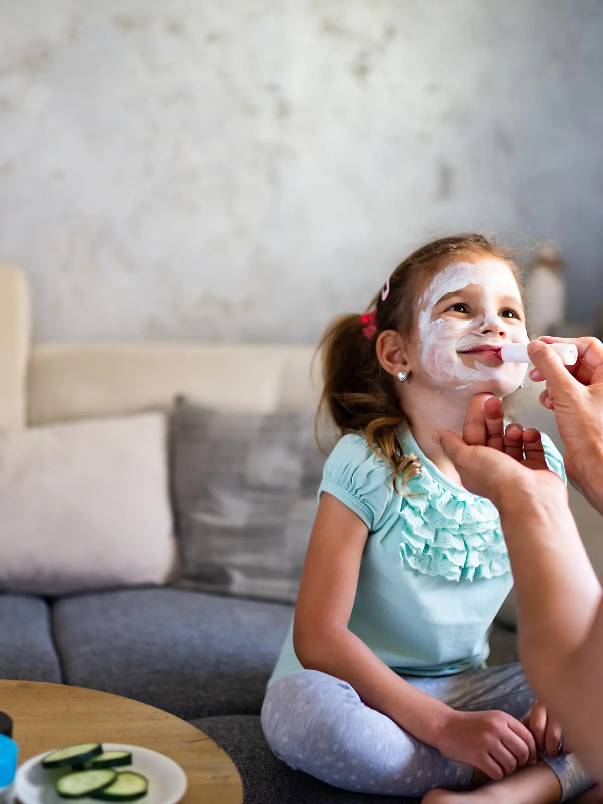 Beautiful woman applying facial mask to daughter’s face. Virtual spa day during COVID-19 isolation.