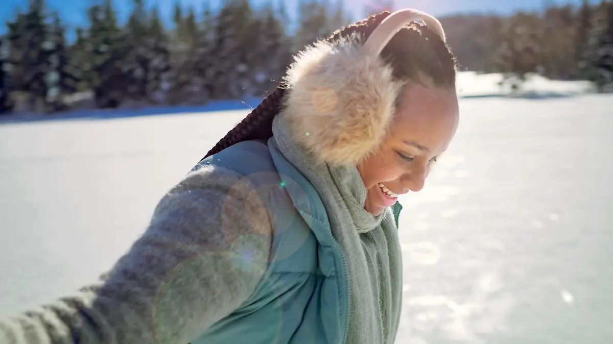 Smiling young woman looking down while ice skating on frozen lake in winter.