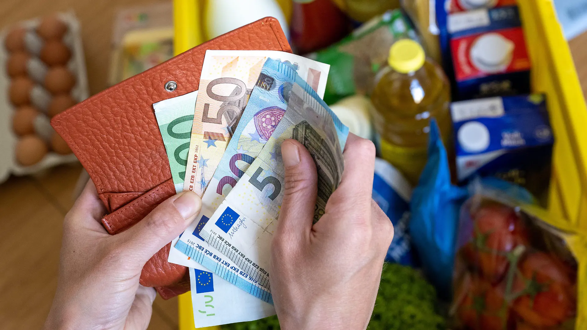 ARCHIV - 02.06.2022, Sachsen, Leipzig: Eine Einkaufskiste mit Lebensmitteln steht auf einem Küchentisch in Leipzig, während eine Frau Euro-Banknoten in den Händen hält. Wie sich die Inflation im Juli entwickelt hat, gibt das Statistische Bundesamt am Donnerstagnachmittag in einer ersten Schätzung bekannt. (zu dpa "Inflation weiter über 7 Prozent - Bundesamt gibt Juli-Daten bekannt") Foto: Hendrik Schmidt/dpa +++ dpa-Bildfunk +++