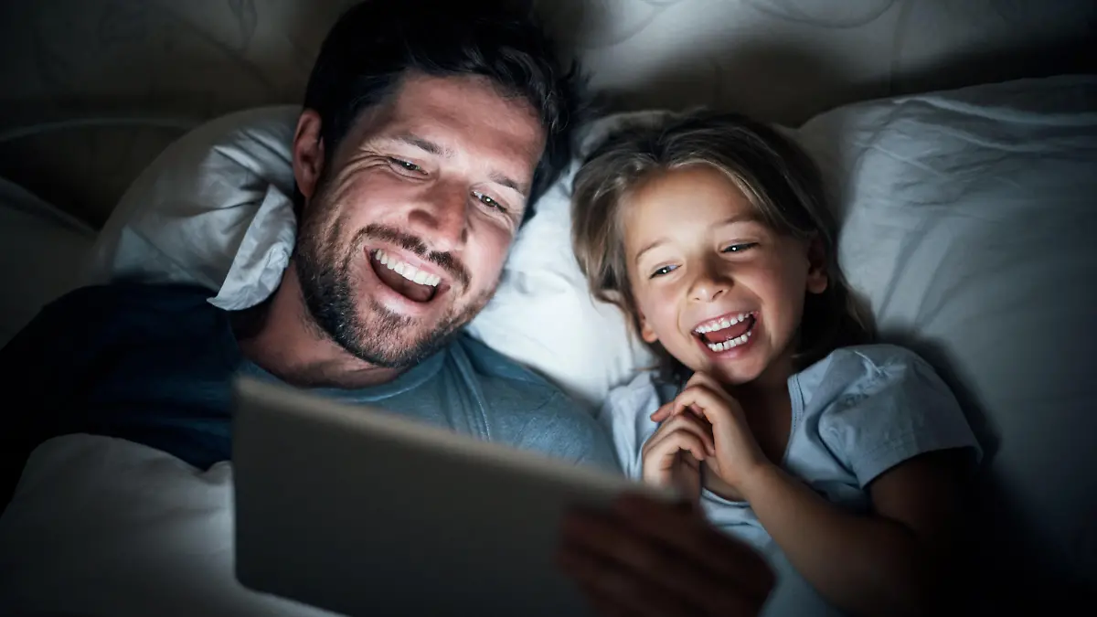 Shot of an adorable little girl and her father using a digital tablet together at night in bed
