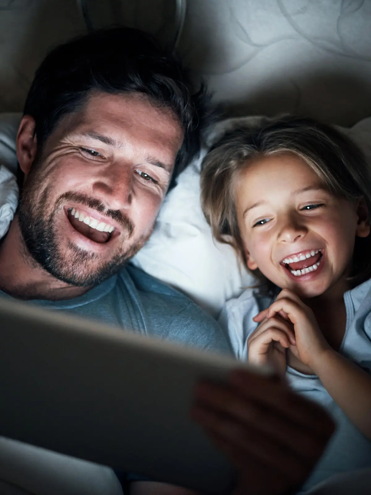 Shot of an adorable little girl and her father using a digital tablet together at night in bed