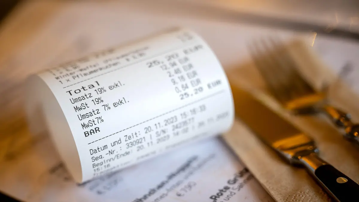 ARCHIV - 20.11.2023, Niedersachsen, Wilhelmshaven: Eine Rechnung mit Umsatzsteuer und Mehrwertsteuer liegt auf der Speisekarte eines Restaurants. (Zu dpa "Mehrwertsteuer auf Speisen im Restaurant steigt wieder auf 19 Prozent.") Foto: Sina Schuldt/dpa +++ dpa-Bildfunk +++