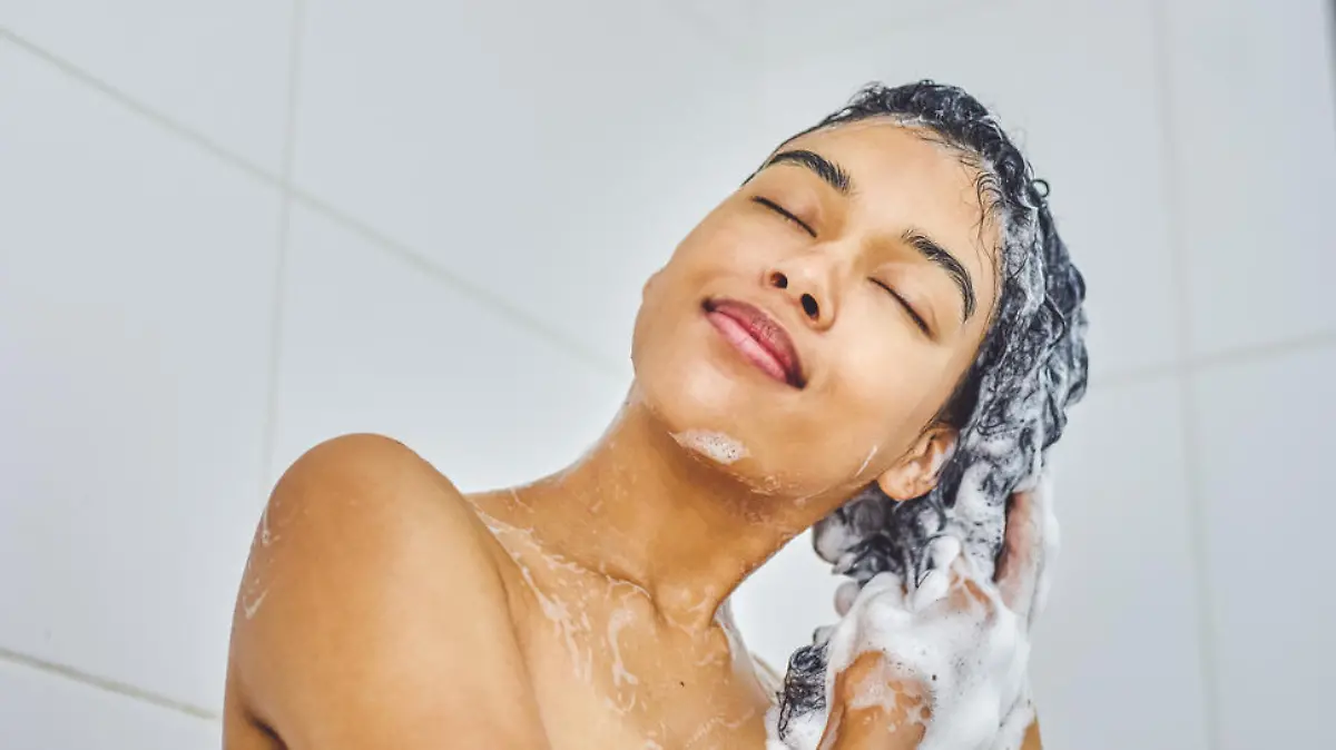 Shot of an attractive young woman washing her hair with shampoo in the shower at home