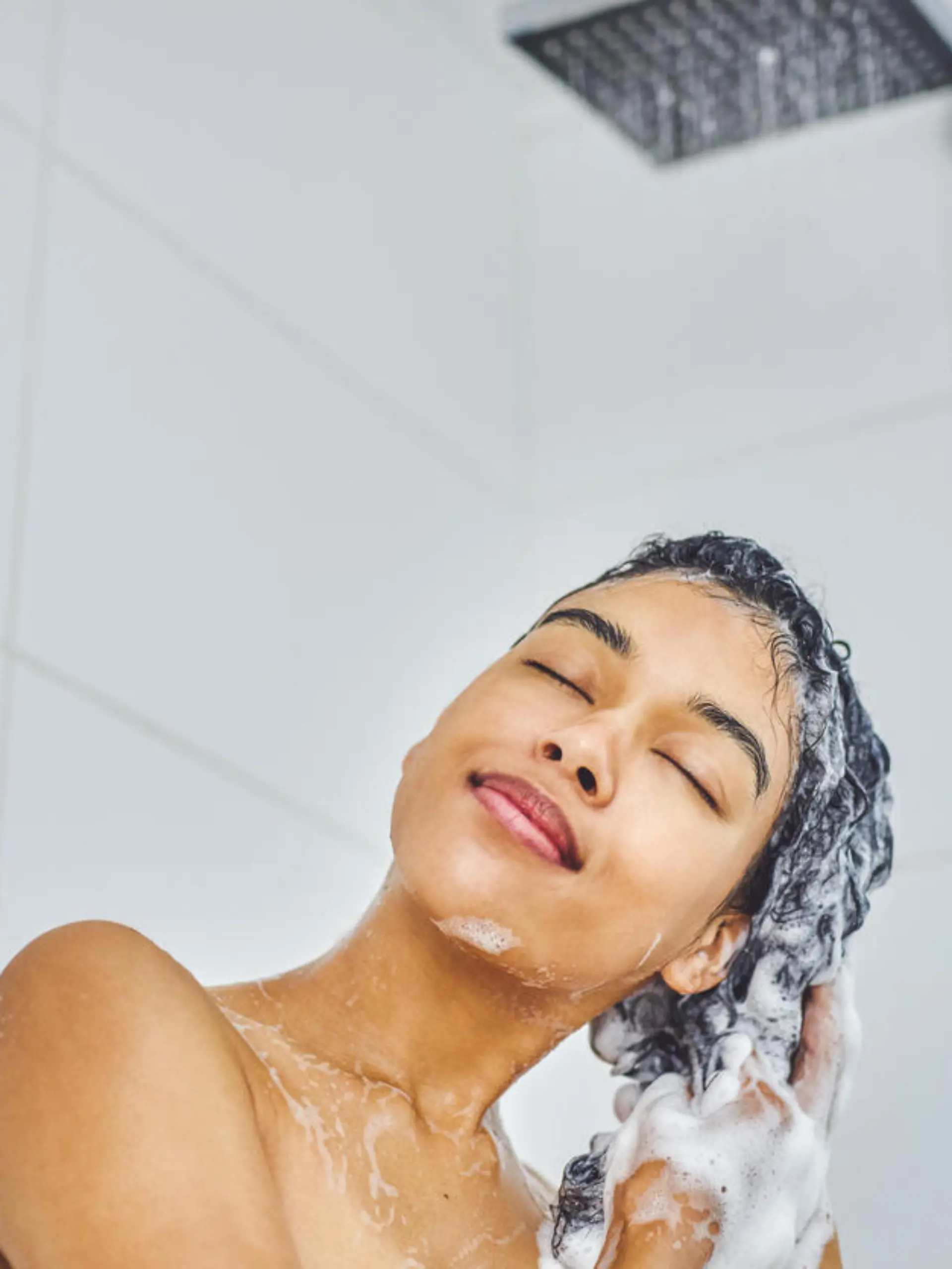 Shot of an attractive young woman washing her hair with shampoo in the shower at home