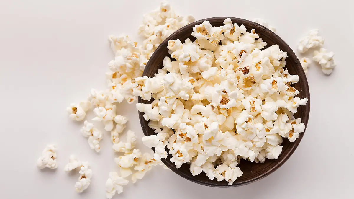 Wooden rustic bowl of popcorn isolated on white background, top view. Fast food, cinema snack and entertainment concept, cutout