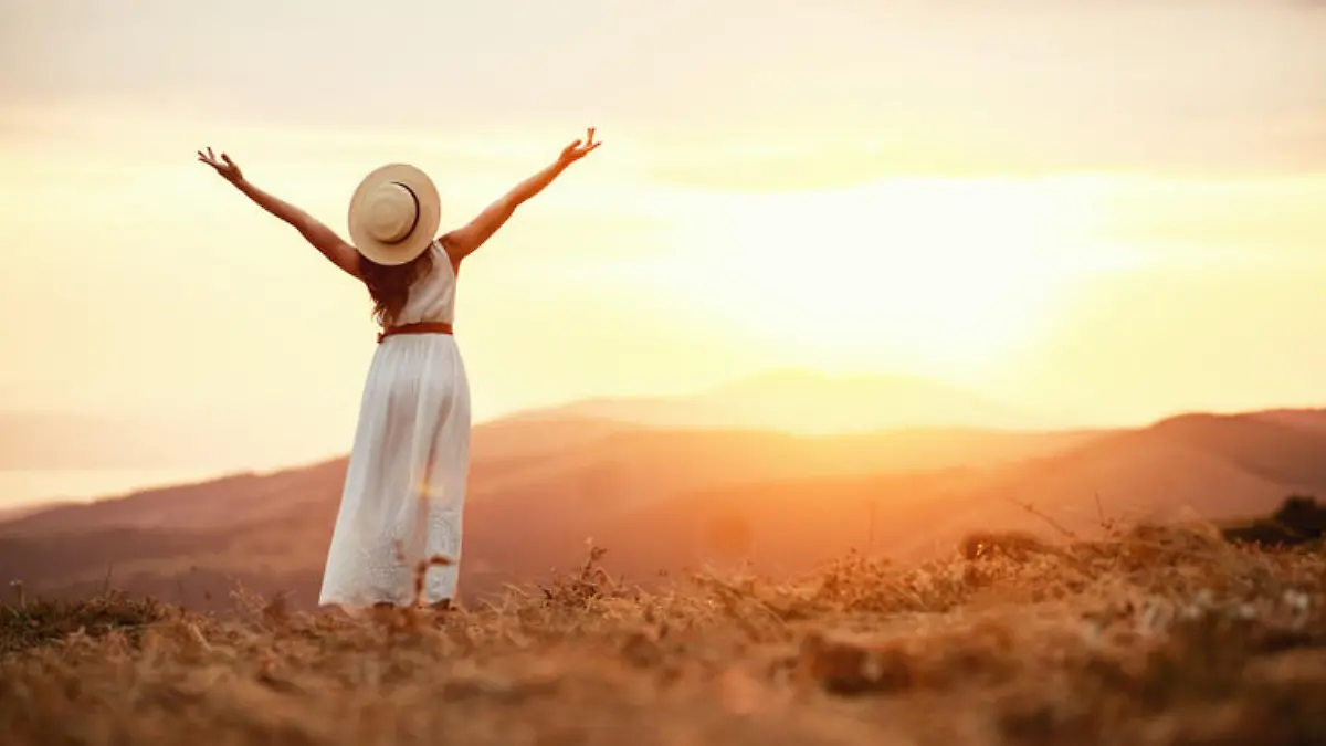Happy woman standing with her back on the sunset in nature in summer