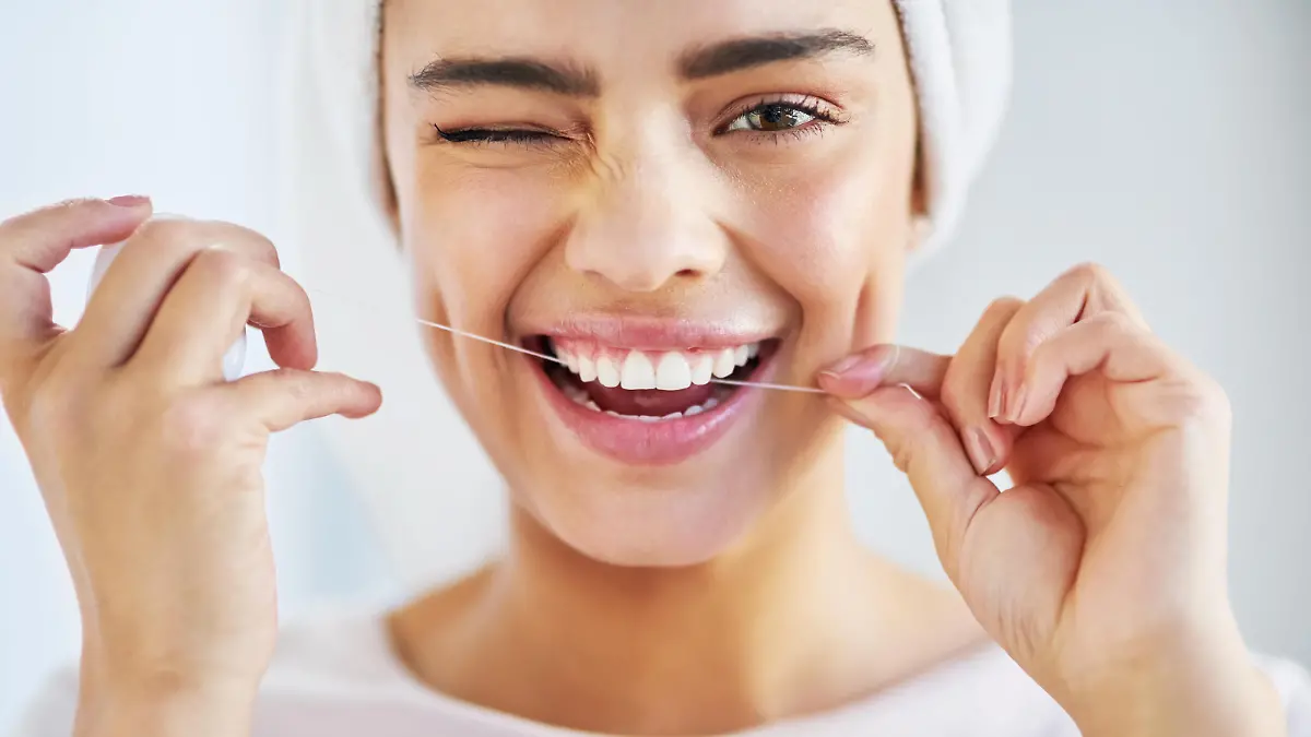 Portrait of a beautiful young woman flossing her teeth in the bathroom at home