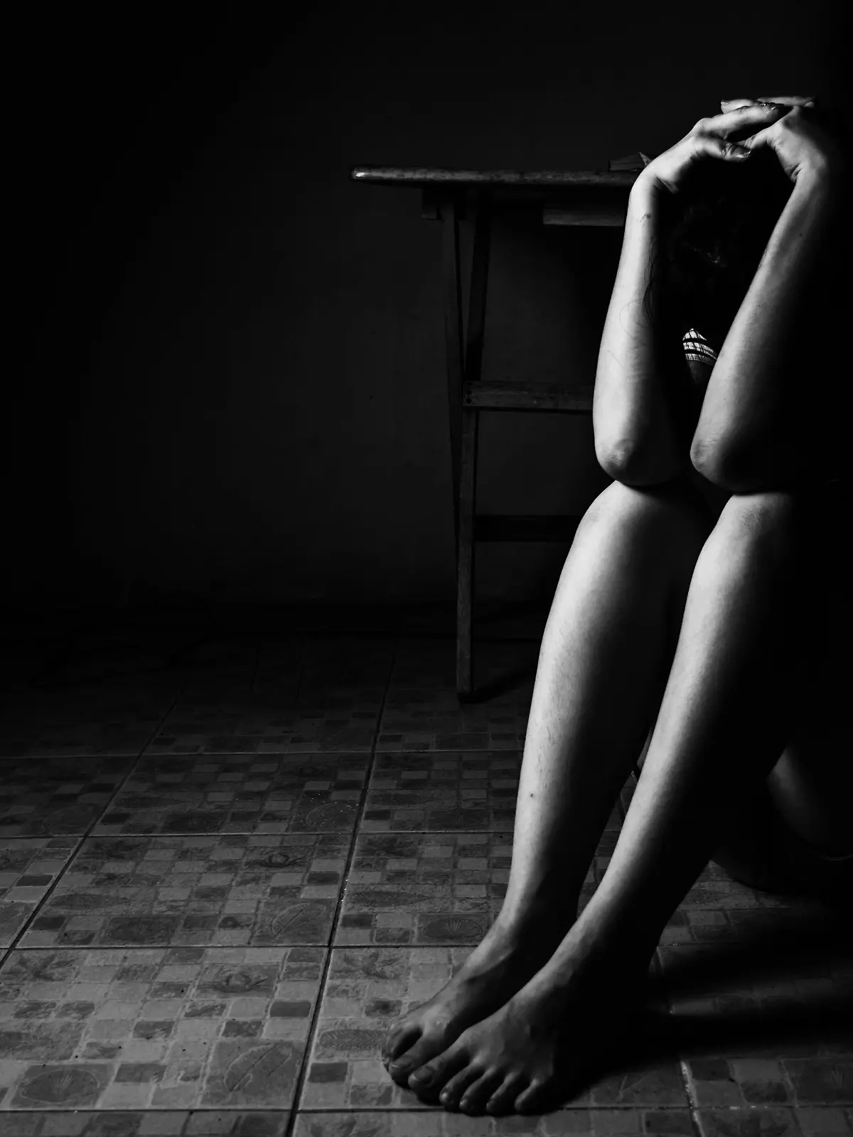 a woman sitting on ground with arm around lower head, sexual violence , sexual abuse, human trafficking concept with shadow edge in white tone