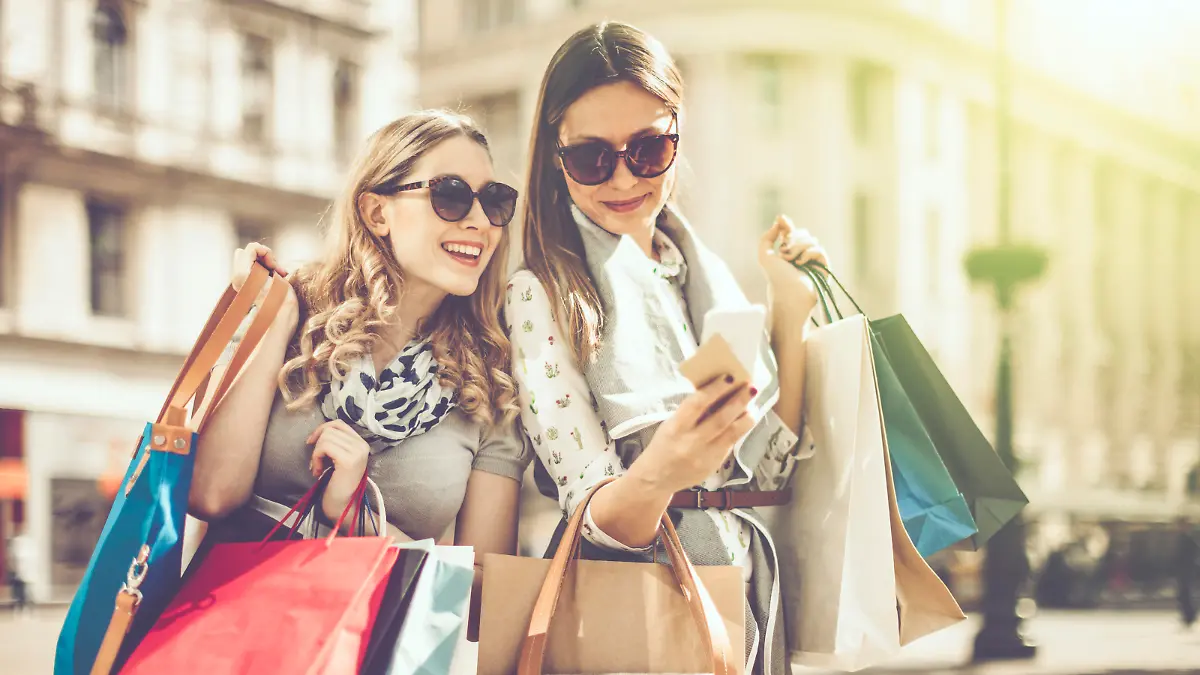 Cheerful beautiful women are shopping in the city. They are using smart phone, and one of them is holding a credit card.