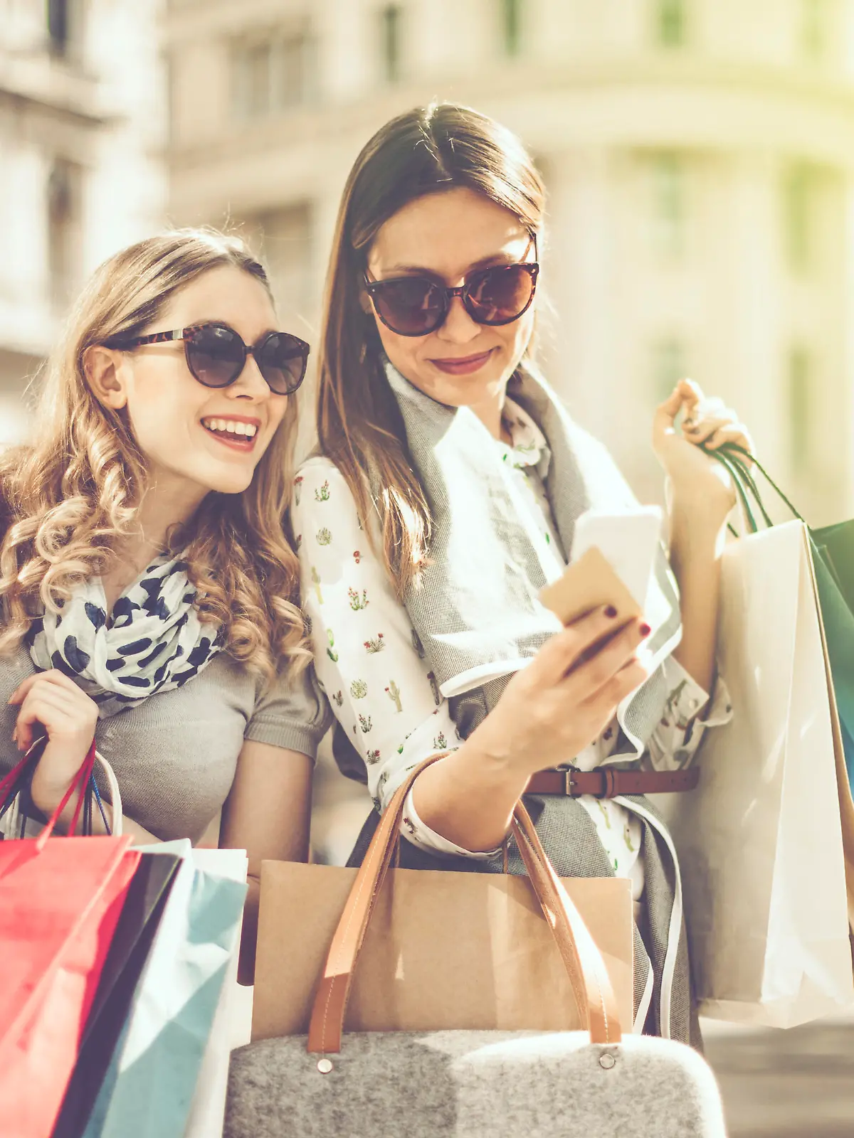 Cheerful beautiful women are shopping in the city. They are using smart phone, and one of them is holding a credit card.
