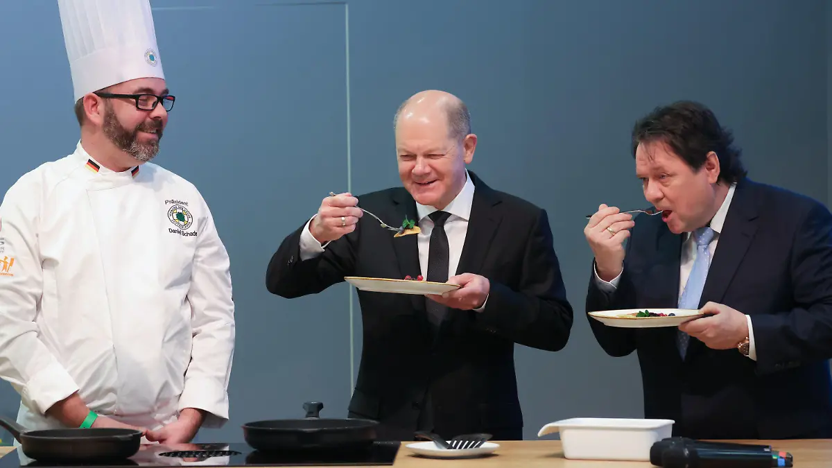 22.01.2024, Berlin: Bundeskanzler Olaf Scholz (SPD, M) probiert neben dem Koch Daniel Schade (l) auf der Grünen Woche einen Pfannkuchen. Vom 19. bis 28. Januar 2024 findet die 88. Ausgabe der Grünen Woche, der internationalen Leitmesse für Ernährung, Landwirtschaft und Gartenbau, statt. Foto: Sean Gallup/Getty Images Pool/dpa +++ dpa-Bildfunk +++