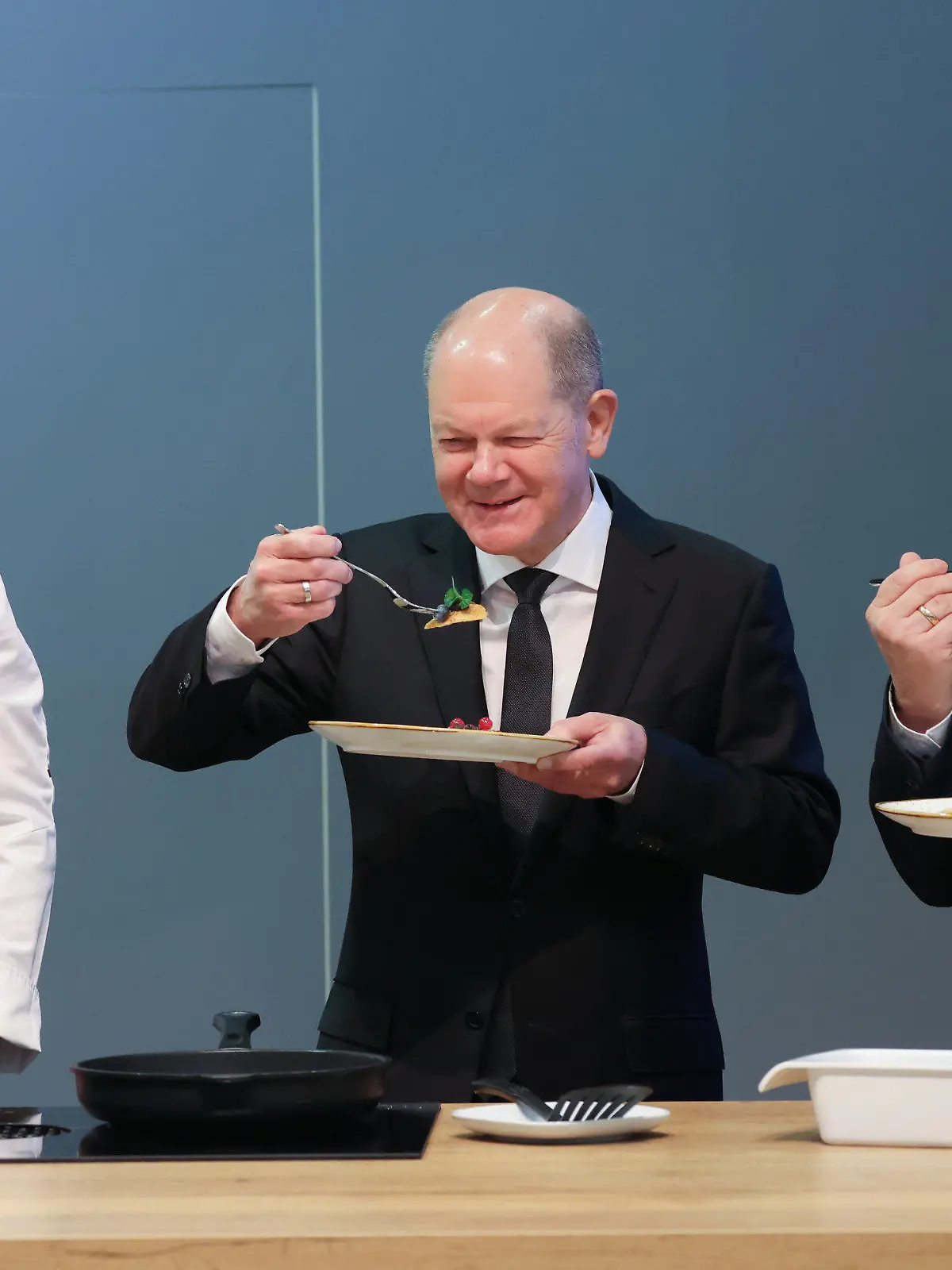 22.01.2024, Berlin: Bundeskanzler Olaf Scholz (SPD, M) probiert neben dem Koch Daniel Schade (l) auf der Grünen Woche einen Pfannkuchen. Vom 19. bis 28. Januar 2024 findet die 88. Ausgabe der Grünen Woche, der internationalen Leitmesse für Ernährung, Landwirtschaft und Gartenbau, statt. Foto: Sean Gallup/Getty Images Pool/dpa +++ dpa-Bildfunk +++
