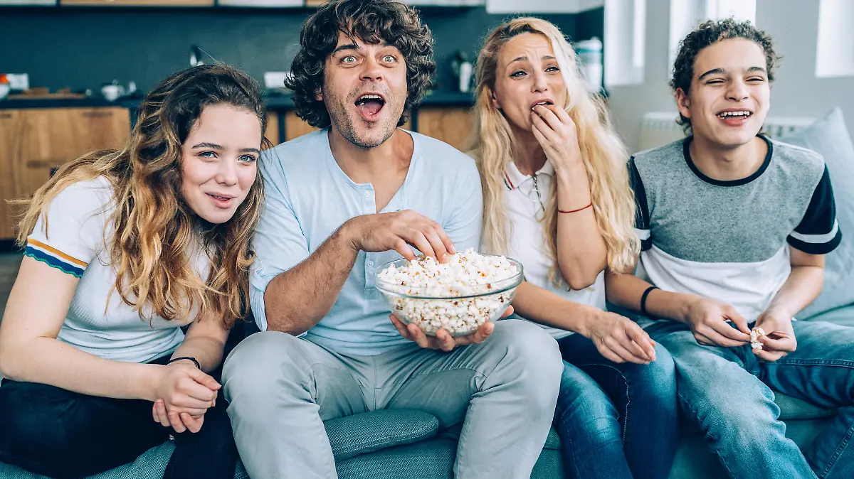Family With Teenage Children Sitting On Sofa, eating popcorn and Watching TV Together