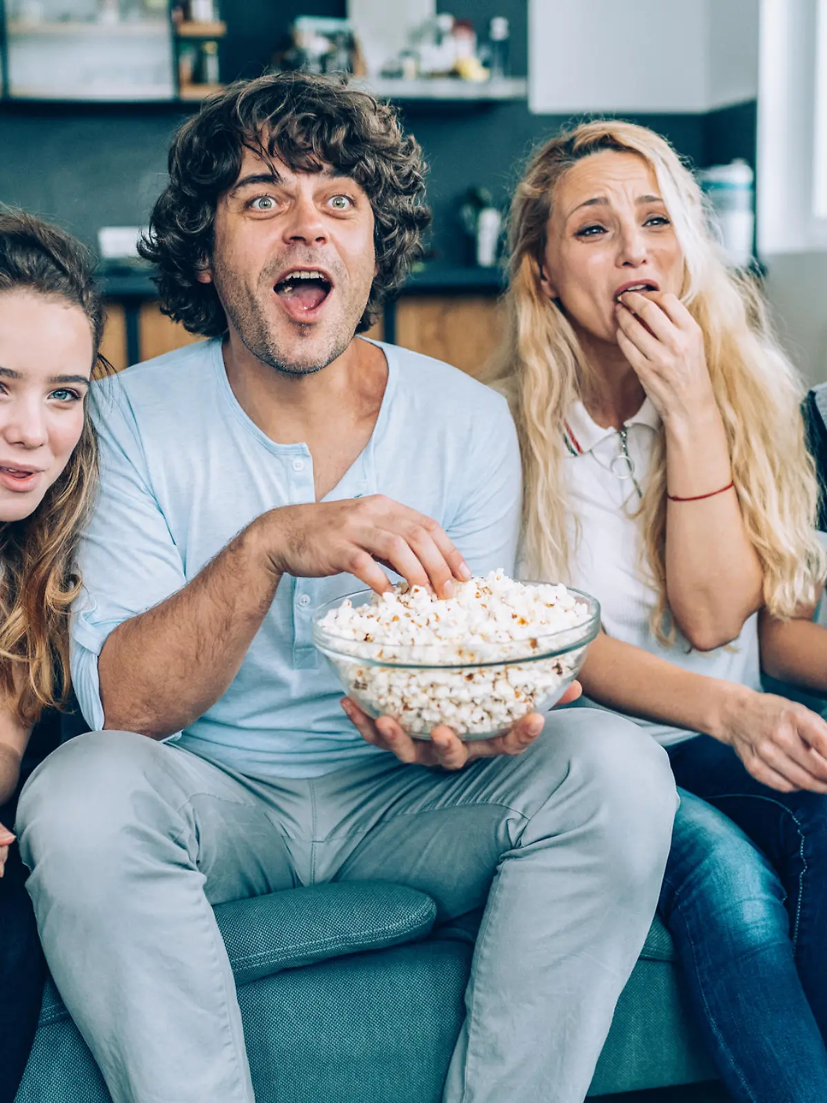 Family With Teenage Children Sitting On Sofa, eating popcorn and Watching TV Together