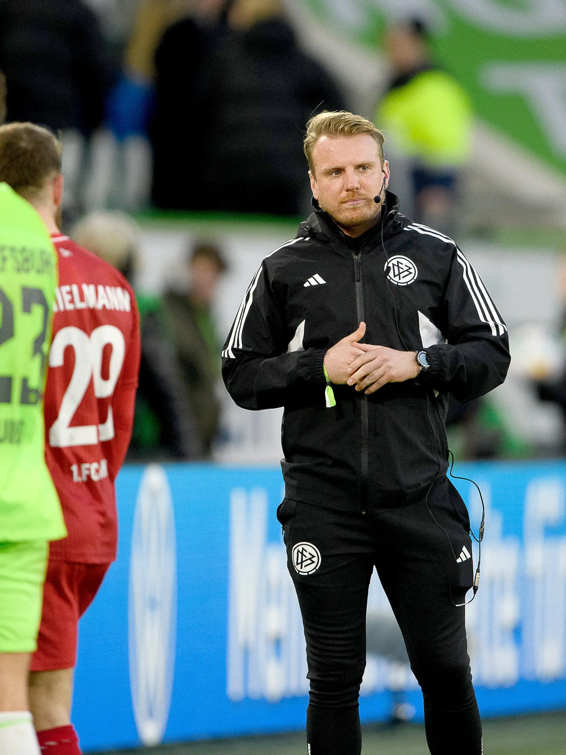 27.01.2024, Niedersachsen, Wolfsburg: Fußball, Bundesliga, VfL Wolfsburg - 1. FC Köln, 19. Spieltag, Volkswagen Arena. Tobias Krull (2.v.r.) übernimmt als ehrenamtlicher Schiedsrichter nach einer Schiedsrichter-Assistenverletzung die Position des vierten Offiziellen. Der frühere Wolfsburger Nachwuchsspieler Tobias Krull ist Torwart und Sportlicher Leiter beim MTV Gifhorn in der Fußball-Landesliga. Er meldete sich während der ersten Halbzeit, als der Stadionsprecher per Lautsprecher-Durchsage jemanden mit Schiedsrichter-Lizenz im Publikum suchte. Es wurde ein Ersatz für das vierte Mitglied des Schiedsrichter-Teams gesucht, das an der Seitenlinie zwischen den beiden Trainern steht. Foto: Swen Pförtner/dpa - WICHTIGER HINWEIS: Gemäß den Vorgaben der DFL Deutsche Fußball Liga bzw. des DFB Deutscher Fußball-Bund ist es untersagt, in dem Stadion und/oder vom Spiel angefertigte Fotoaufnahmen in Form von Sequenzbildern und/oder videoähnlichen Fotostrecken zu verwerten bzw. verwerten zu lassen. +++ dpa-Bildfunk +++