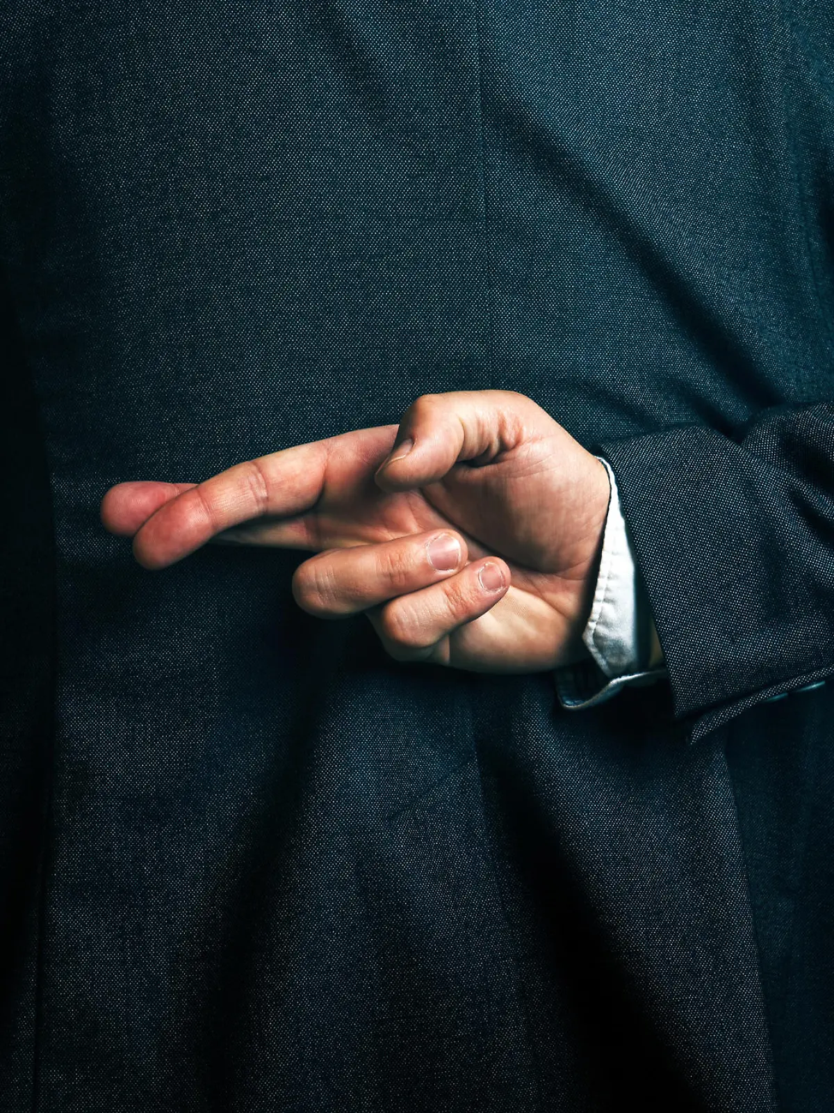 Dishonest businessman telling lies, lying businessperson holding fingers crossed behind his back