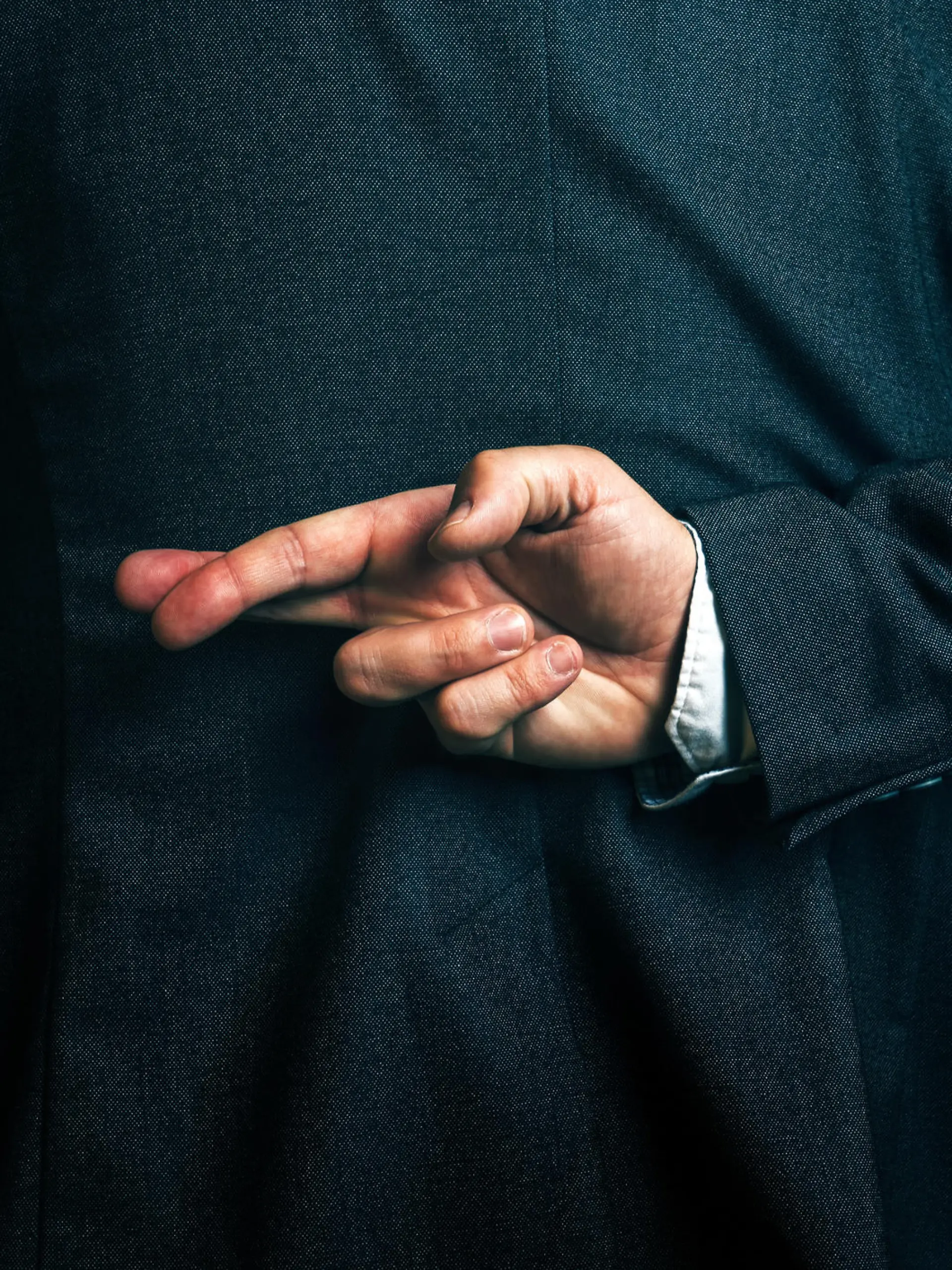 Dishonest businessman telling lies, lying businessperson holding fingers crossed behind his back