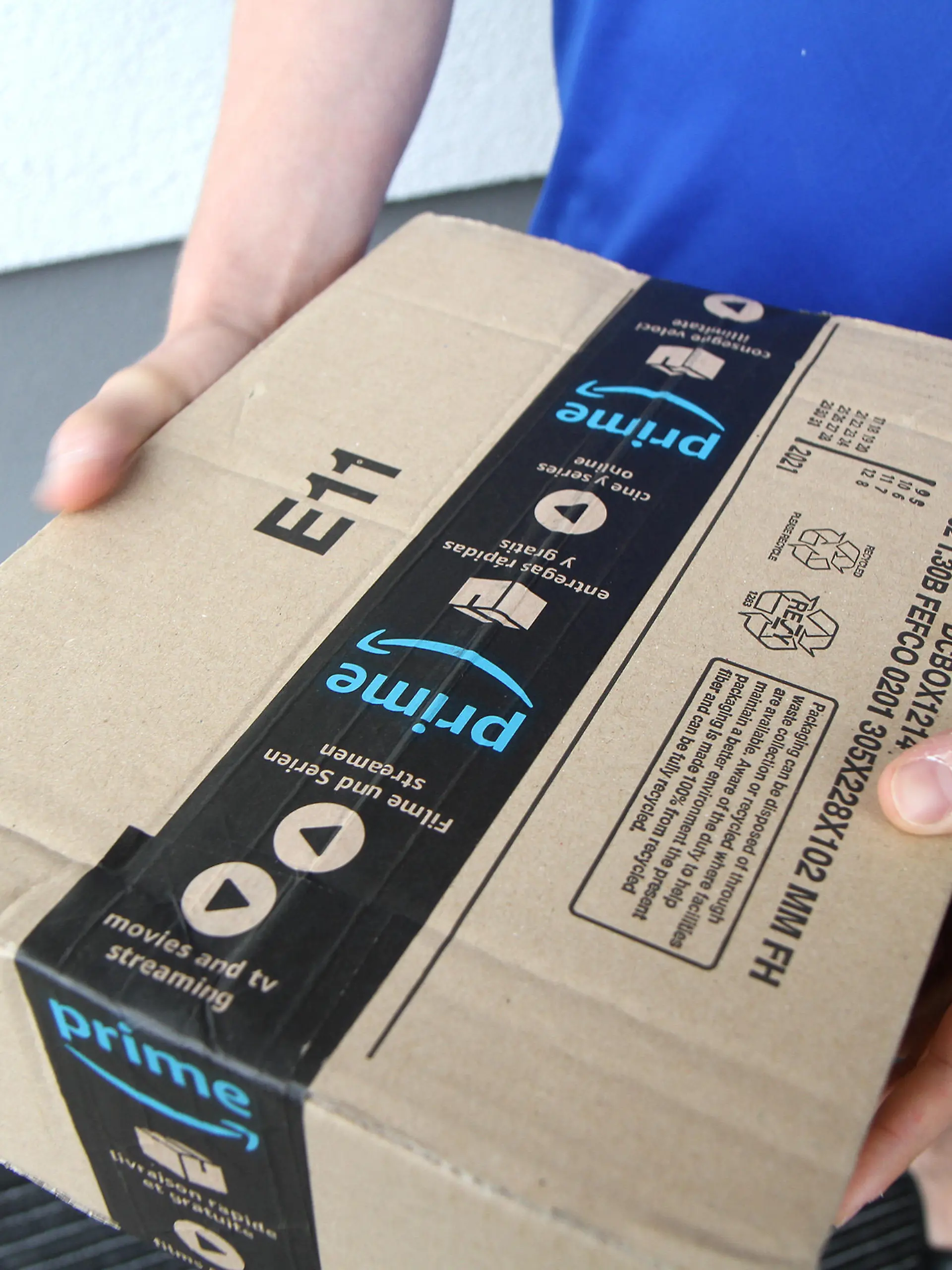 Themenbild - Paketzustellung, Paketanlieferung Amazon Prime, Prime, Logo Bild: Eine Person hat ein Paket von Amazon Prime in der Hand das vor der Haustür zugestellt wird. Themenbild, Featurebild, Symbolbild