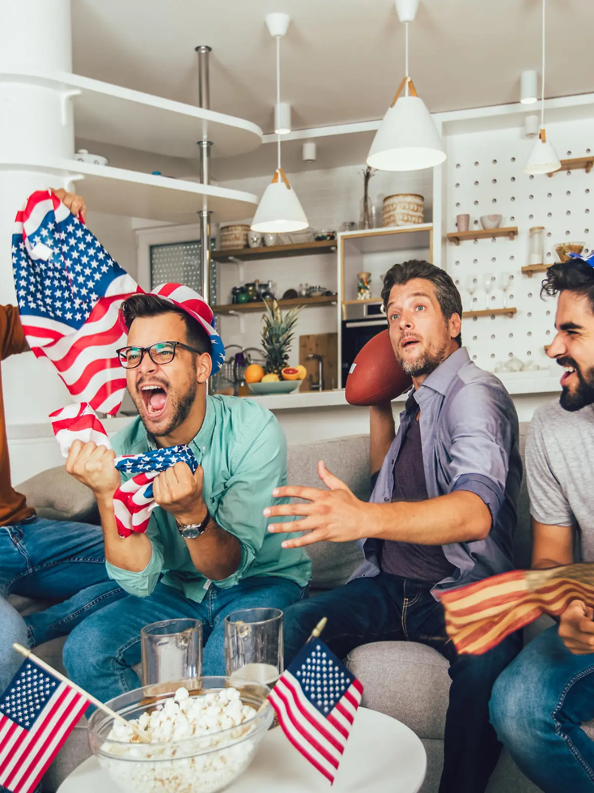 Excited male friends cheering while watching American football match on sofa at home.