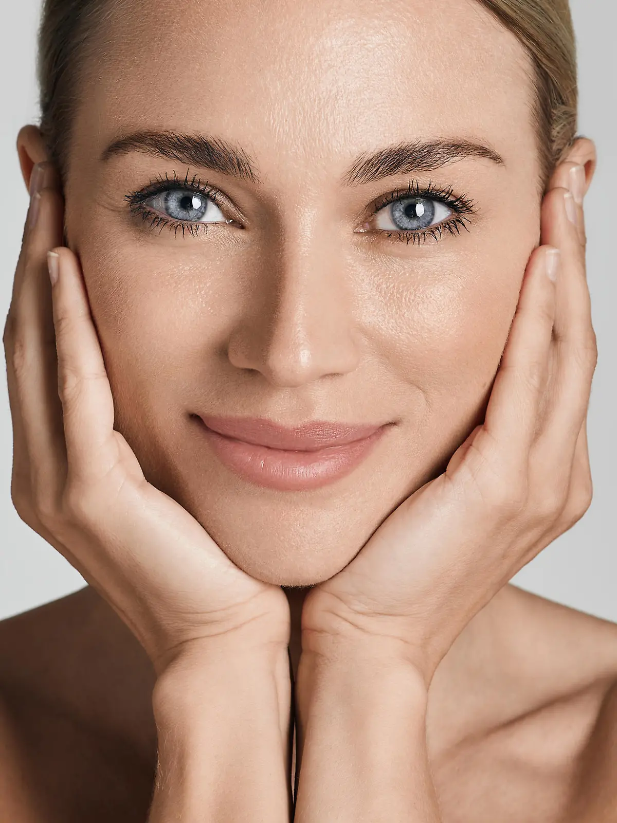 Skin care. Beautiful woman with healthy facial skin touching hands moisturized face skin, on light grey background. High quality