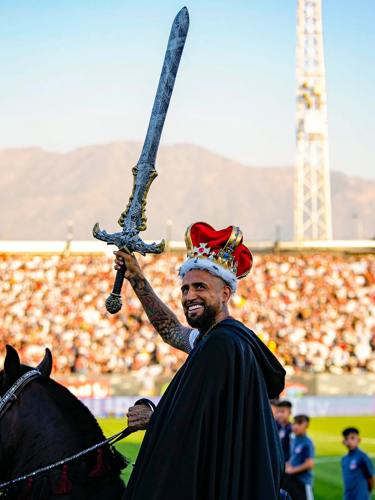 Chilean soccer player Arturo Vidal waves a sword while riding a horse on to the pitch at his welcoming event at the Monumental Stadium in Santiago, Chile, Thursday, Feb. 1, 2024. Vidal returns to play for Colo Colo after 17 years of a successful career playing for soccers clubs in Europe and South America. (AP Photo/Esteban Felix)