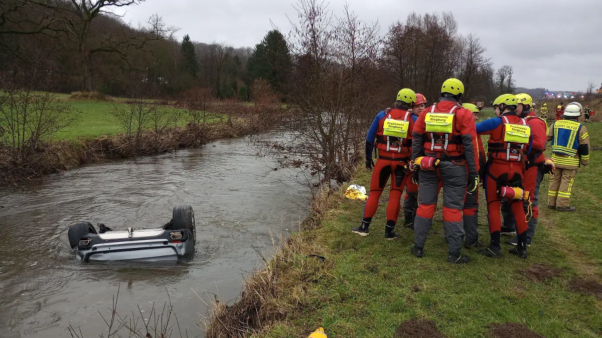 04.02.2024, Nordrhein-Westfalen, Lohmar: Feuerwehrleute stehen neben einem Auto im Fluss Sülz. Ein Autofahrer hat am Sonntag mit seinem Wagen auf der Autobahn 3 bei Lohmar eine Leitplanke durchbrochen und ist in den Fluss Sülz gestürzt. Dort blieb das Fahrzeug kopfüber im Wasser liegen. Retter bargen aus dem Inneren den 25 Jahre alten lebensgefährlich verletzten Fahrer und eine schwer verletzte 24 Jahre alte Beifahrerin, wie ein Polizeisprecher mitteilte. Foto: Marius Fuhrmann/dpa +++ dpa-Bildfunk +++