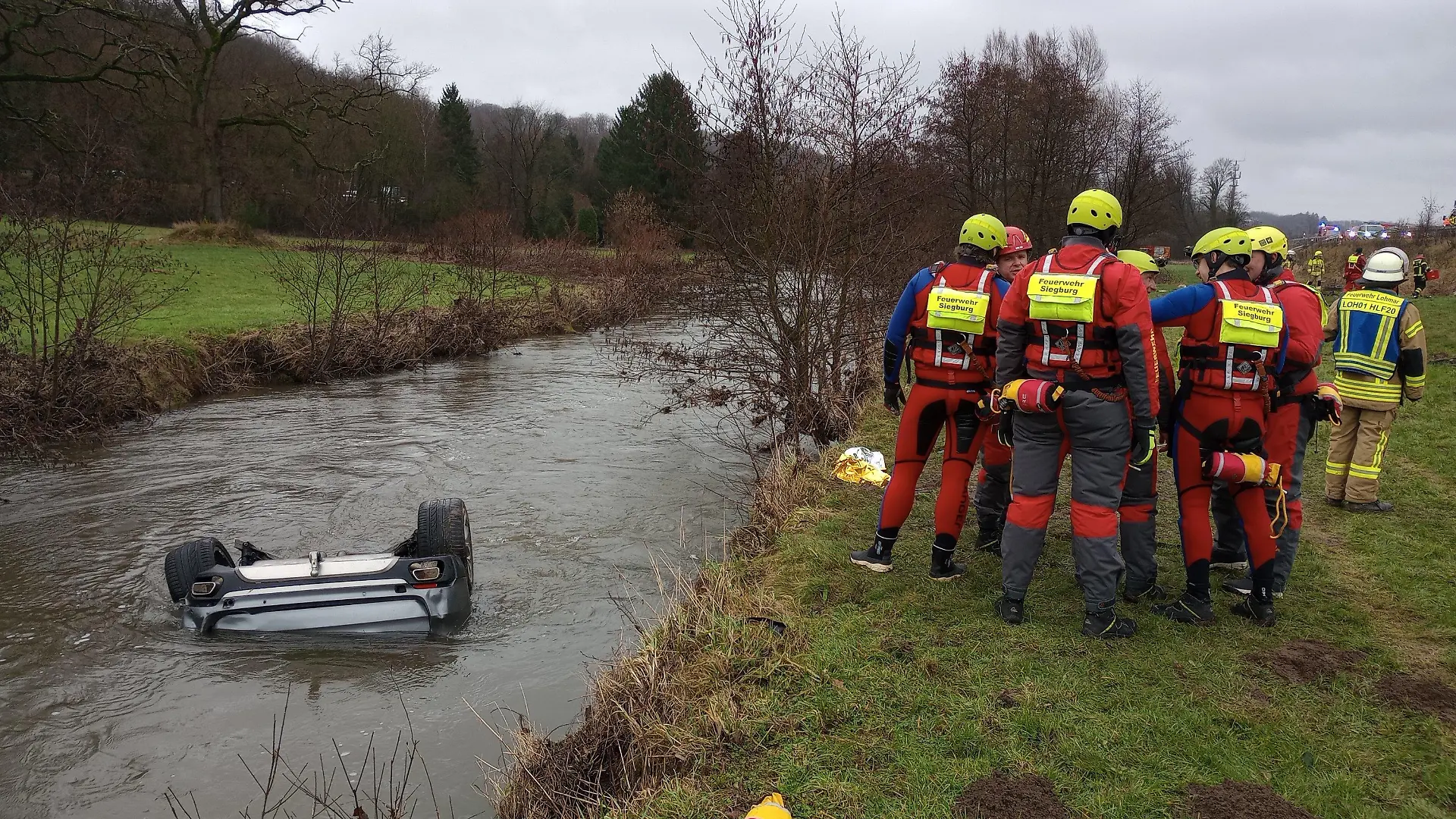 04.02.2024, Nordrhein-Westfalen, Lohmar: Feuerwehrleute stehen neben einem Auto im Fluss Sülz. Ein Autofahrer hat am Sonntag mit seinem Wagen auf der Autobahn 3 bei Lohmar eine Leitplanke durchbrochen und ist in den Fluss Sülz gestürzt. Dort blieb das Fahrzeug kopfüber im Wasser liegen. Retter bargen aus dem Inneren den 25 Jahre alten lebensgefährlich verletzten Fahrer und eine schwer verletzte 24 Jahre alte Beifahrerin, wie ein Polizeisprecher mitteilte. Foto: Marius Fuhrmann/dpa +++ dpa-Bildfunk +++