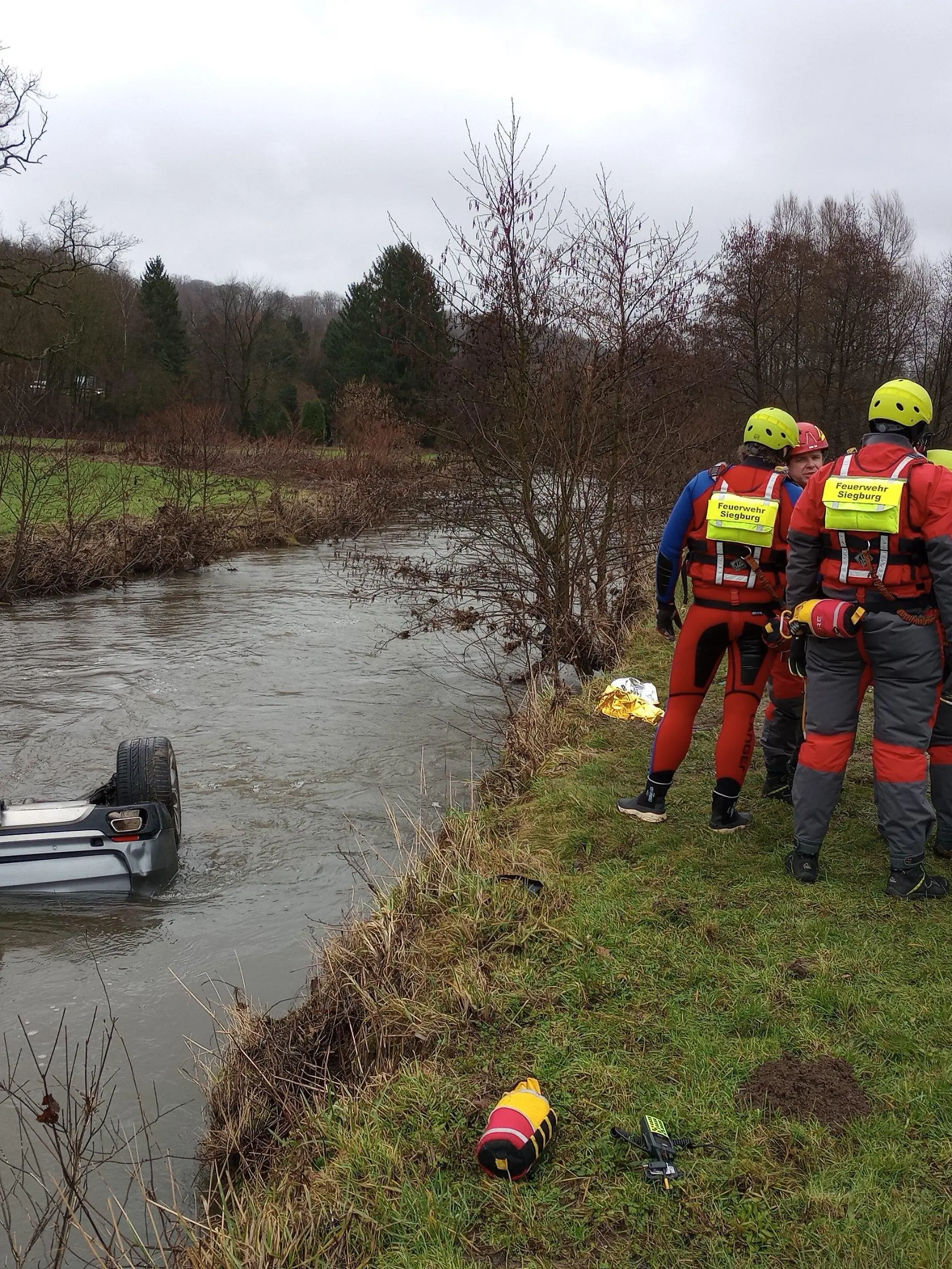 04.02.2024, Nordrhein-Westfalen, Lohmar: Feuerwehrleute stehen neben einem Auto im Fluss Sülz. Ein Autofahrer hat am Sonntag mit seinem Wagen auf der Autobahn 3 bei Lohmar eine Leitplanke durchbrochen und ist in den Fluss Sülz gestürzt. Dort blieb das Fahrzeug kopfüber im Wasser liegen. Retter bargen aus dem Inneren den 25 Jahre alten lebensgefährlich verletzten Fahrer und eine schwer verletzte 24 Jahre alte Beifahrerin, wie ein Polizeisprecher mitteilte. Foto: Marius Fuhrmann/dpa +++ dpa-Bildfunk +++