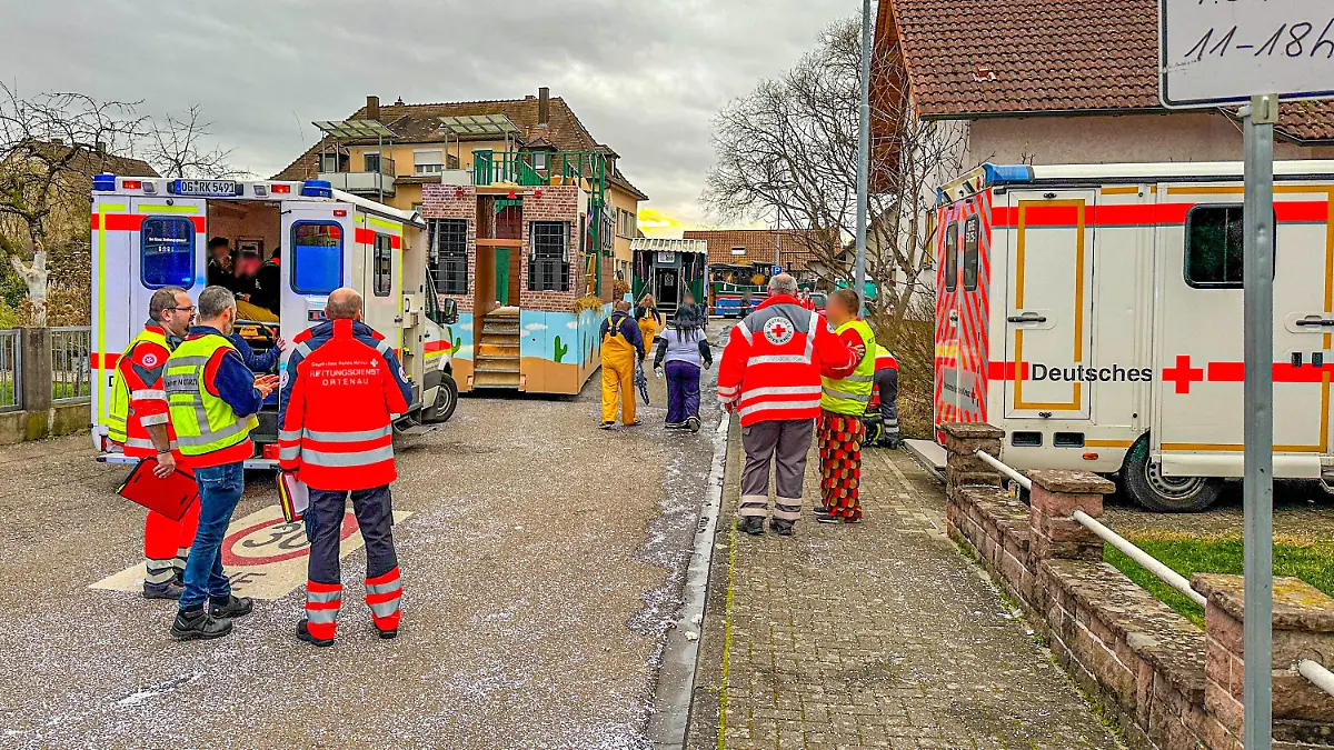 04.02.2024, Baden-Württemberg, Kehl: Rettungswagen, Karnevalisten und Einsatzkräfte stehen in der Nähe der Unfallstelle. Bei einem Faschingsumzug im baden-württembergischen Kehl ist am Sonntag ein Faschingswagen in Brand geraten. Foto: Marco Dürr/Einsatzreport24/dpa +++ dpa-Bildfunk +++
