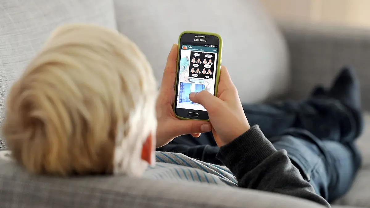 Ein Kind liegt auf einem Sofa und blickt auf sein Smartphone.