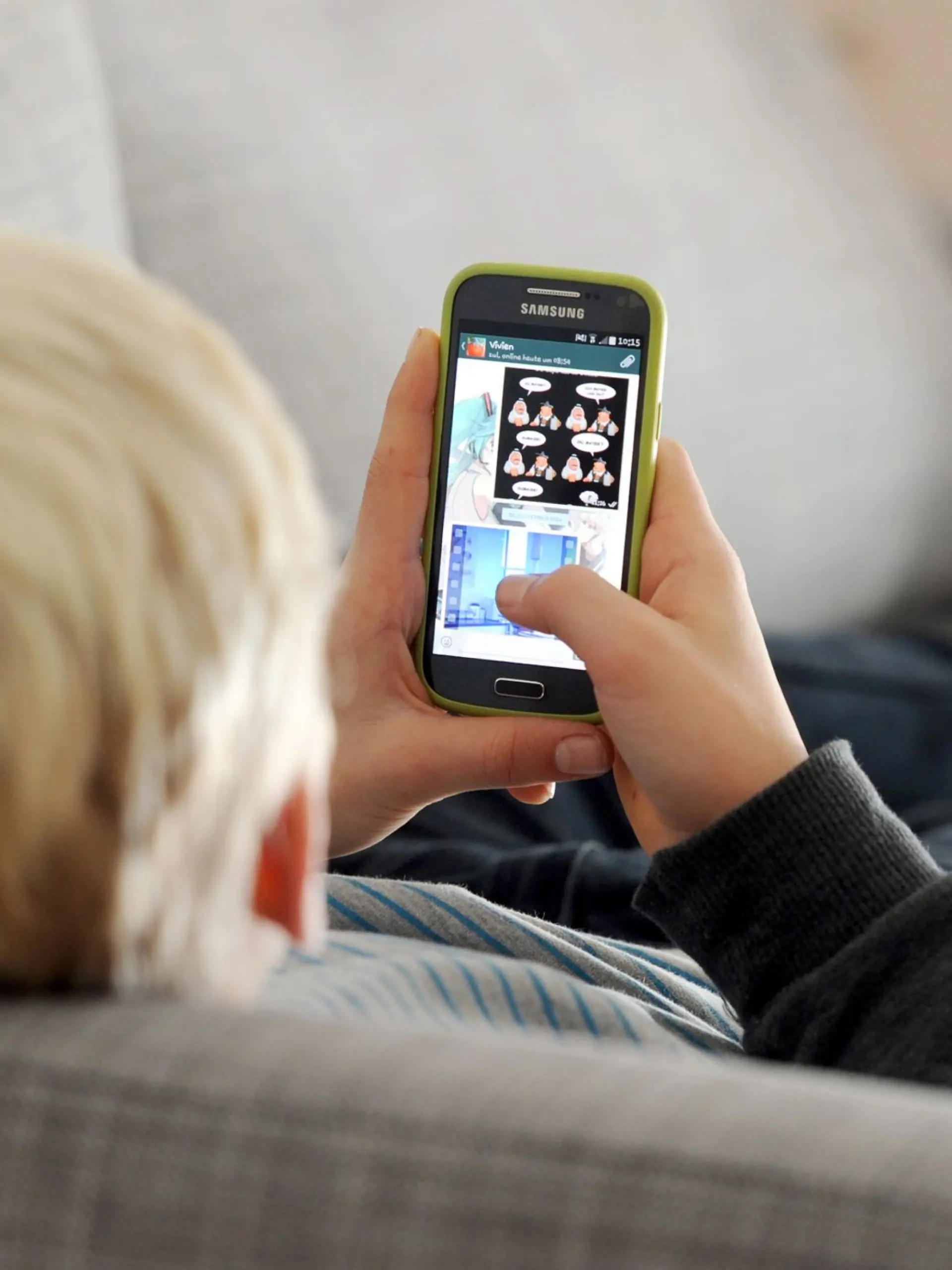 Ein Kind liegt auf einem Sofa und blickt auf sein Smartphone.