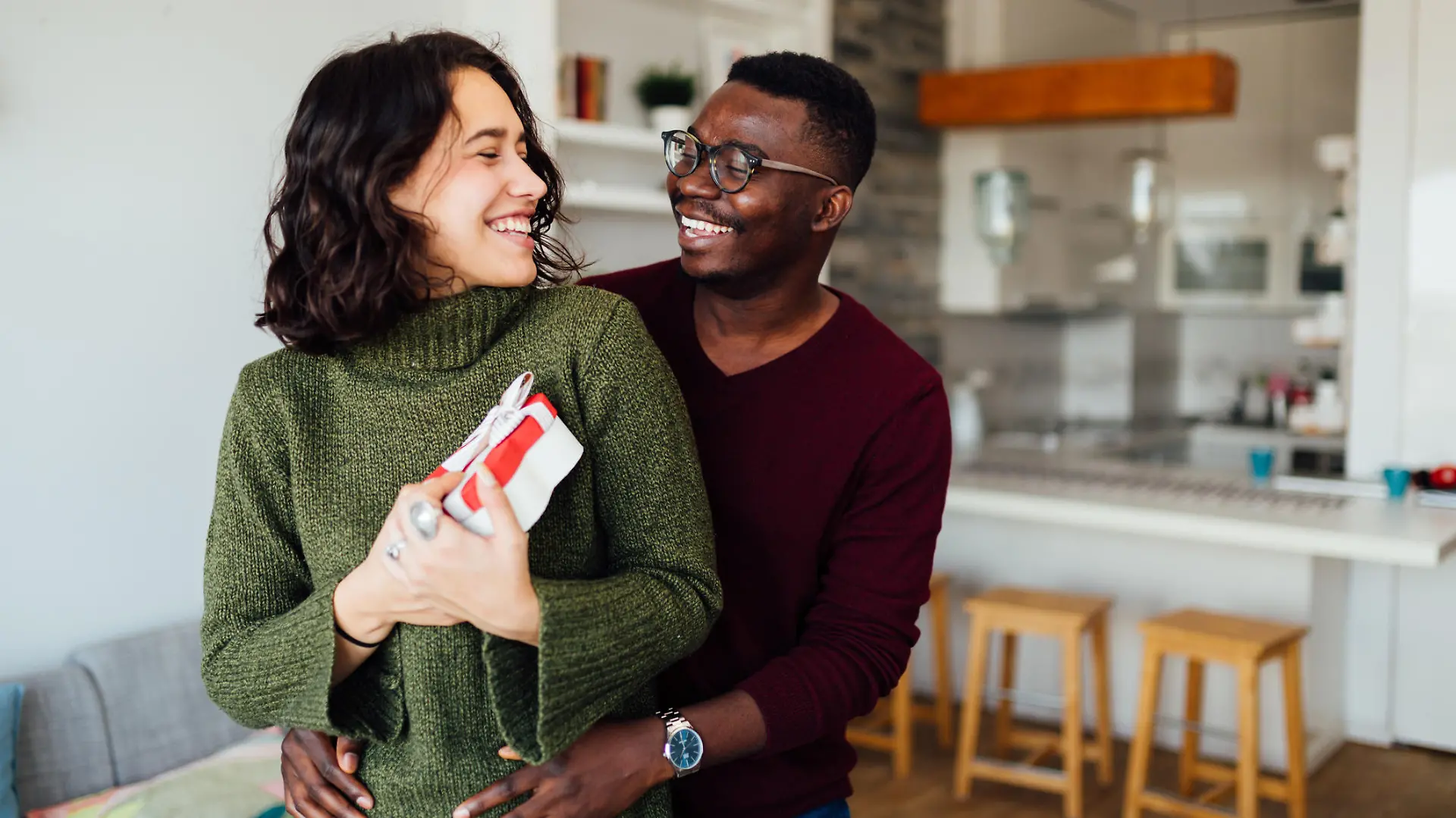 Happy young interracial couple having fun at home, African American boyfriend surprising his Caucasian girlfriend with a Valentine''s day present, making her smile