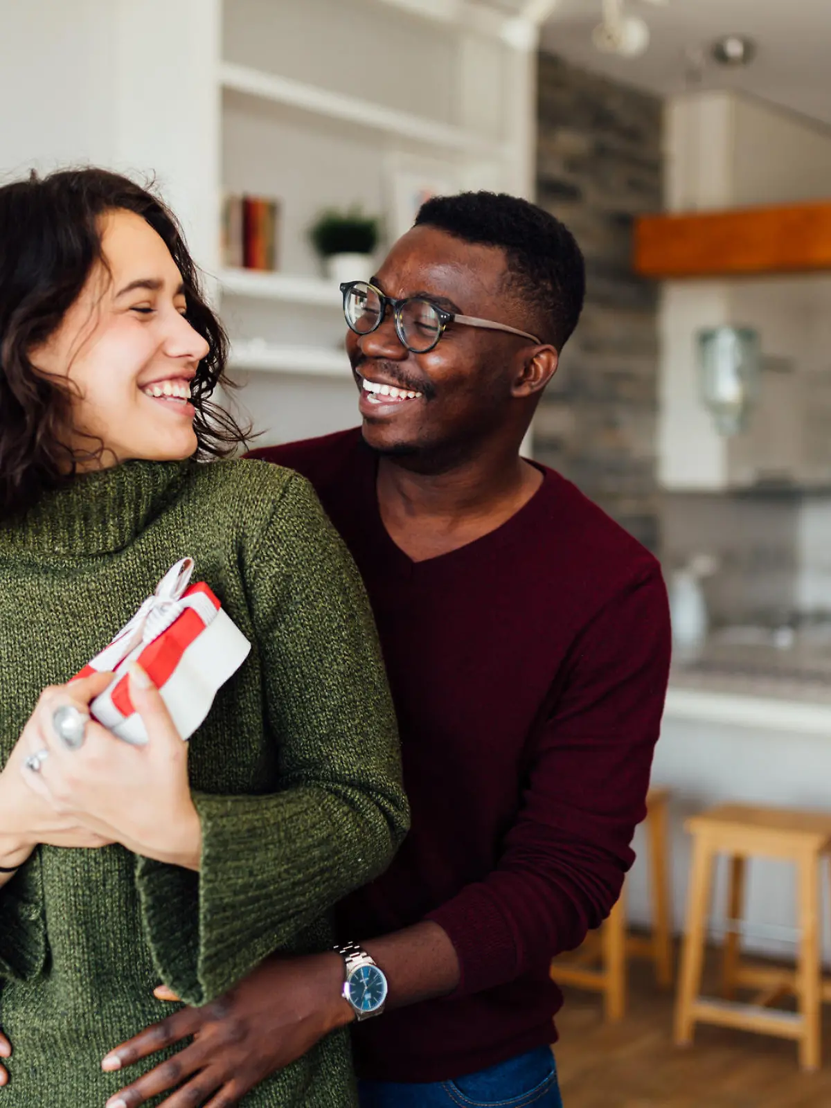 Happy young interracial couple having fun at home, African American boyfriend surprising his Caucasian girlfriend with a Valentine''s day present, making her smile