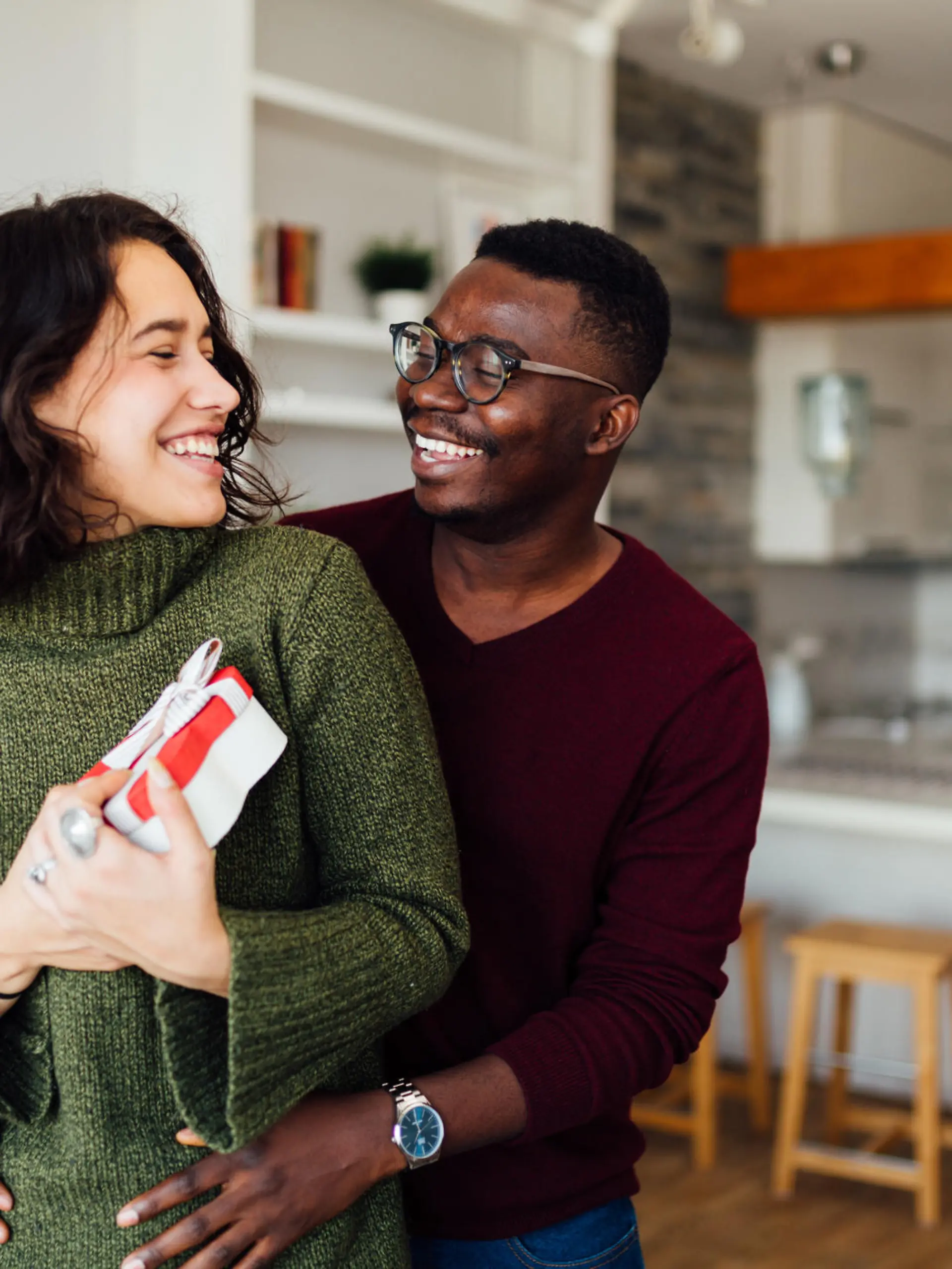 Happy young interracial couple having fun at home, African American boyfriend surprising his Caucasian girlfriend with a Valentine''s day present, making her smile