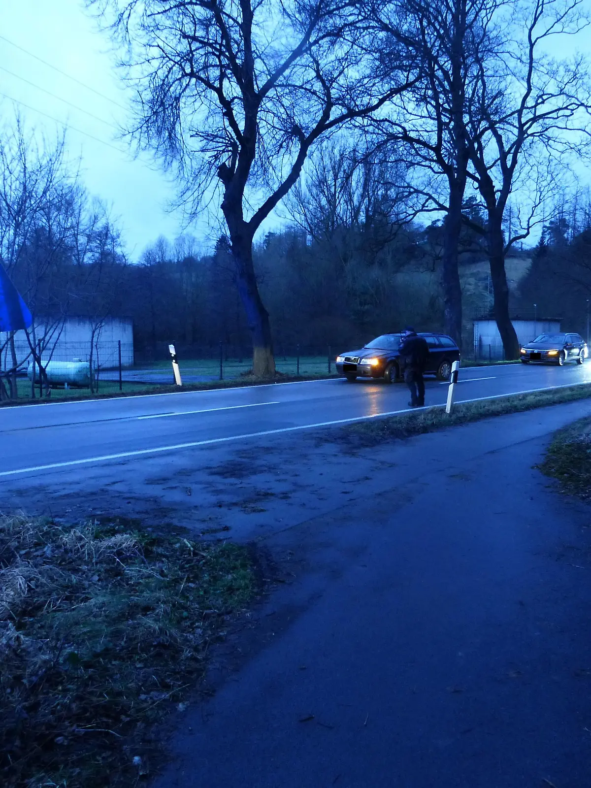 Auf dieser Landstraße wurde ein 8-Jähriges Mädchen von einem Auto erfasst. Der dunkelblaue Unfallwagen kann nicht mehr bremsen, als das Mädchen auf die Straße läuft.