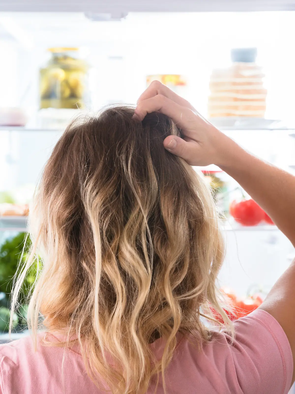 Rear View Of A Confused Woman Looking In Open Refrigerator At Home