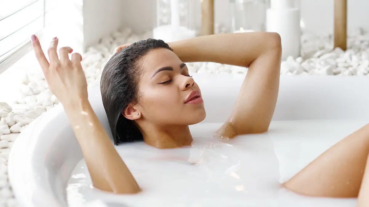 Sexy woman with glass of beverage in bath with milk. Female person in bathtub, beauty and health care in spa, wellness treathment in bathroom, pebbles and candles on background