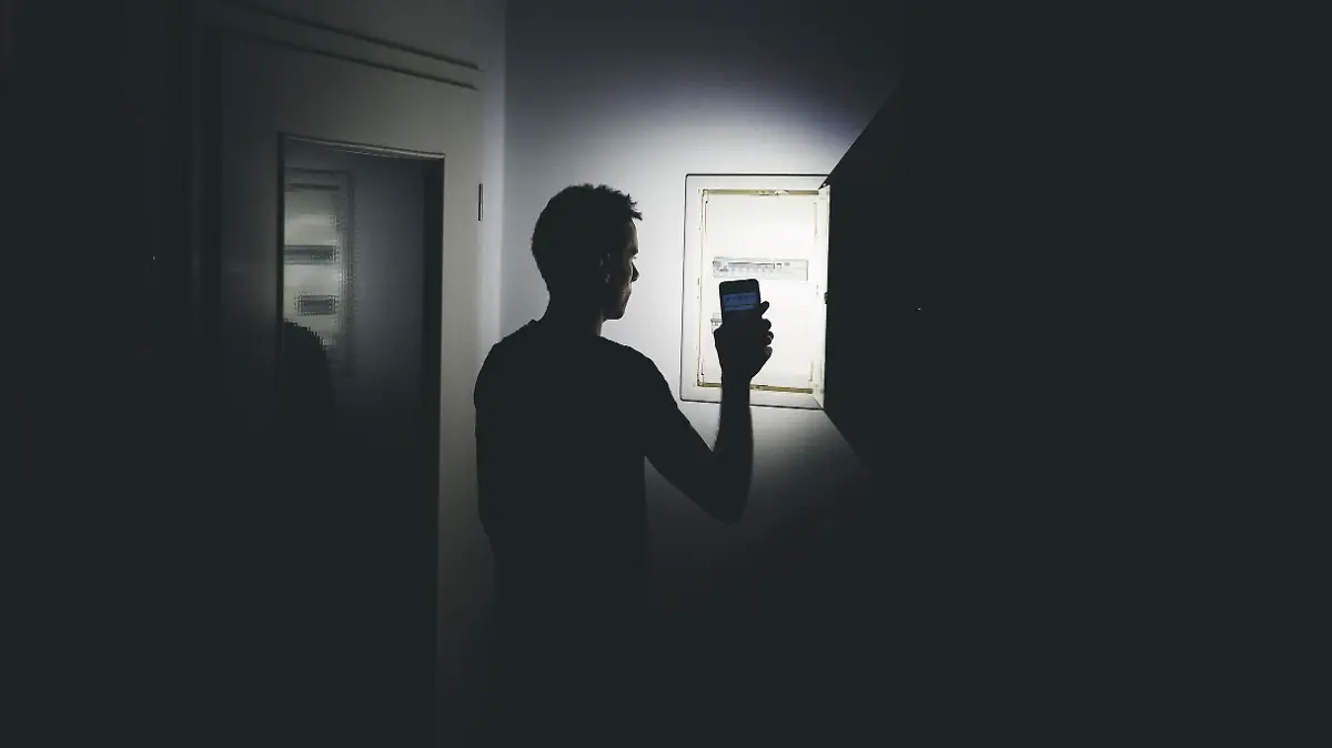 Stromausfall in der Wohnung, Mann leuchtet mit der Taschenlampe in seinem Smartphone in der dunklen Wohnung und überprüft den Sicherungskasten. Elektrizität, Strom Ausfall, Blackout Konzept