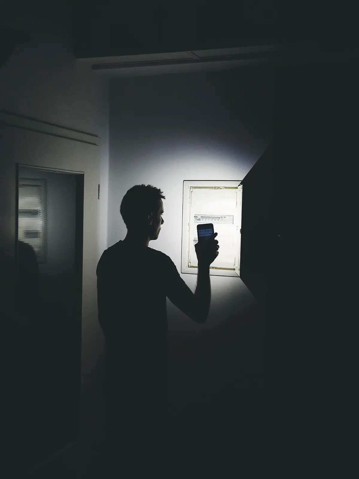 Stromausfall in der Wohnung, Mann leuchtet mit der Taschenlampe in seinem Smartphone in der dunklen Wohnung und überprüft den Sicherungskasten. Elektrizität, Strom Ausfall, Blackout Konzept
